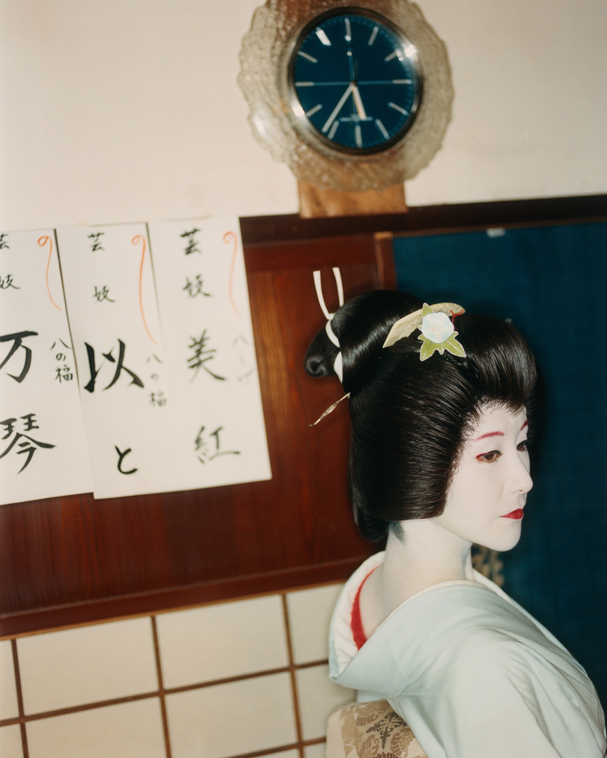 Mikou, a 24 year-old geisha, at Hachishige tea house before her performance, with banners on the wall displaying the names of the geishas who work there.