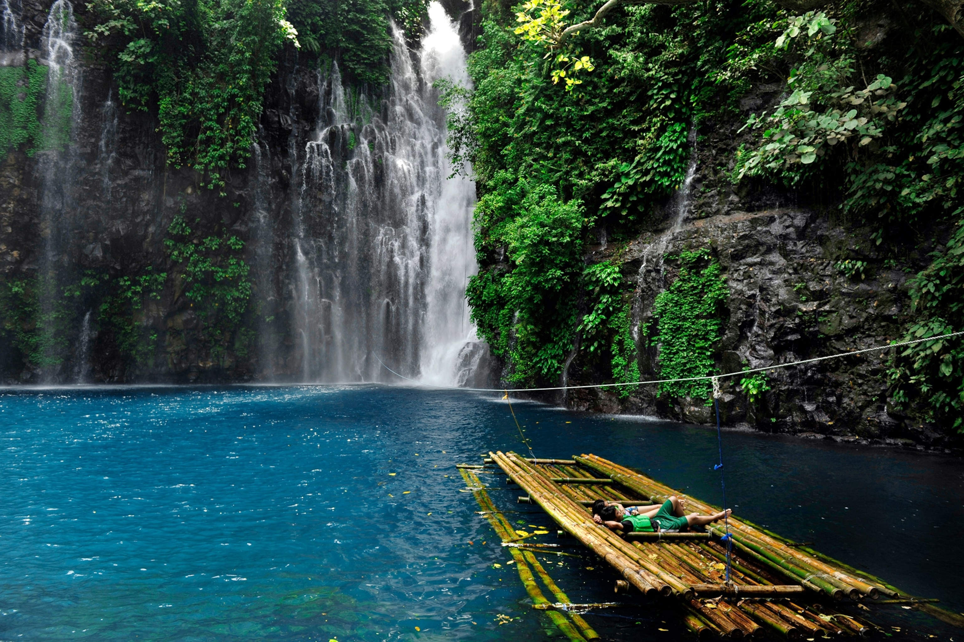 bathers lazing on a bamboo raft at the Tinago Falls in the Philippines