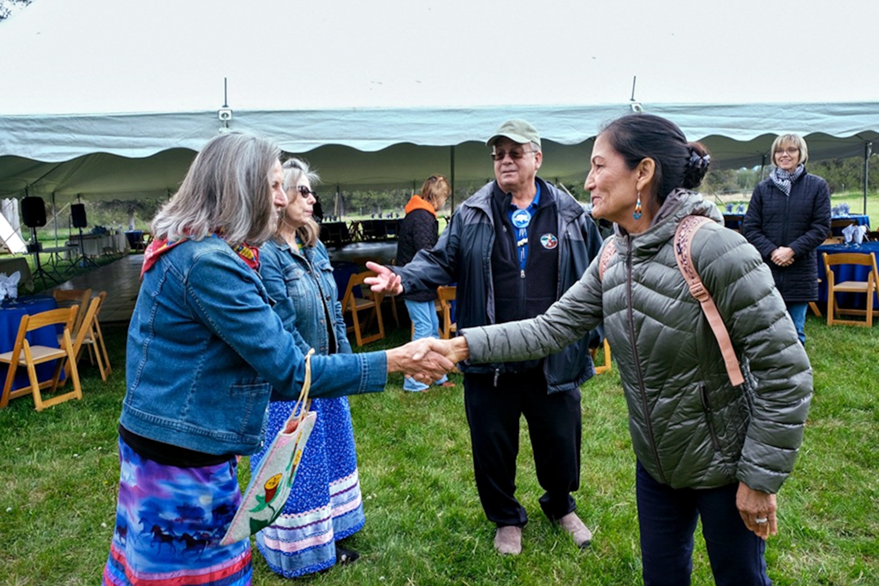 Woman in blue puffy coat shaking hands with another woman when other people watching them.