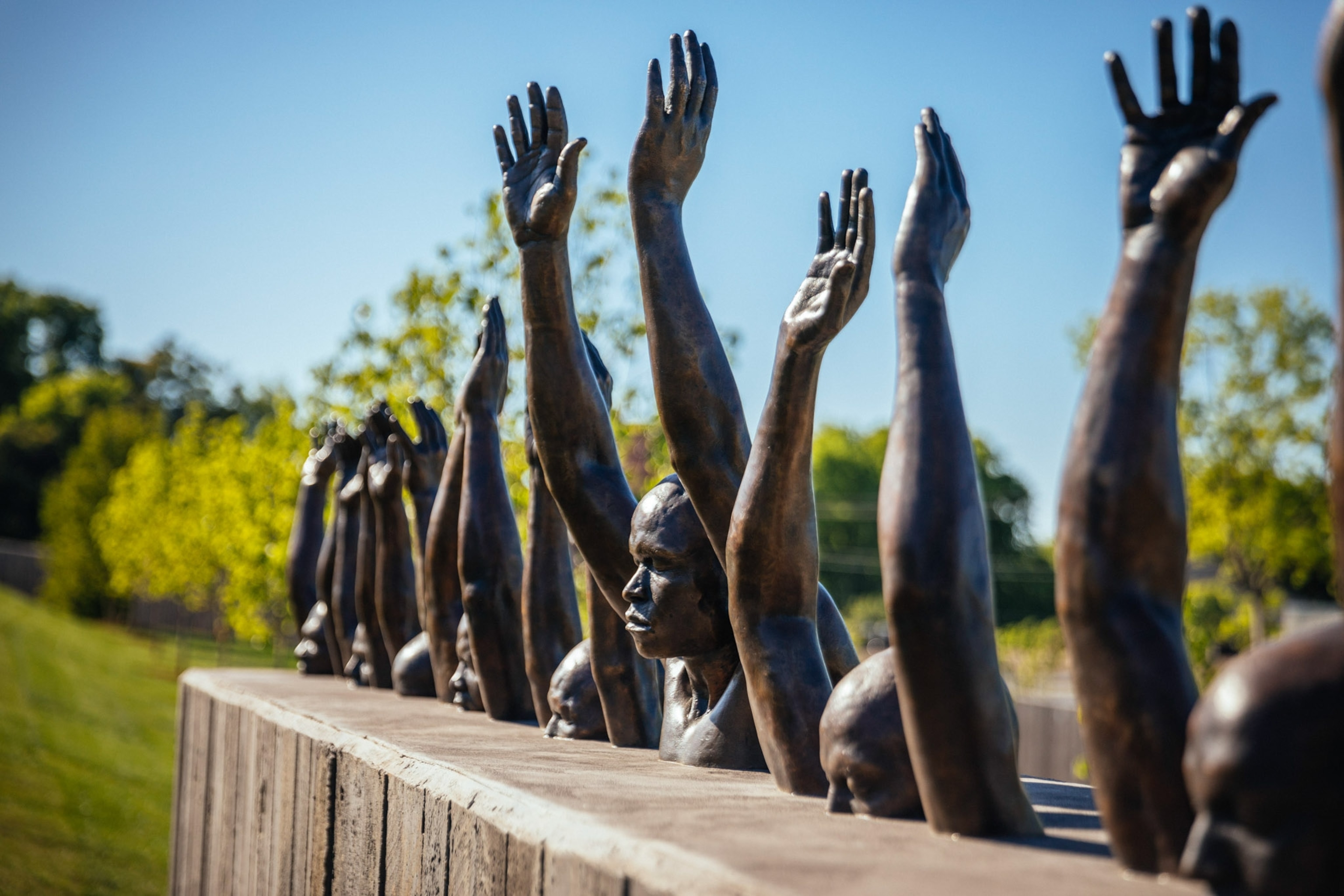 A bronze sculpture of busts with their hands raised outdoors.