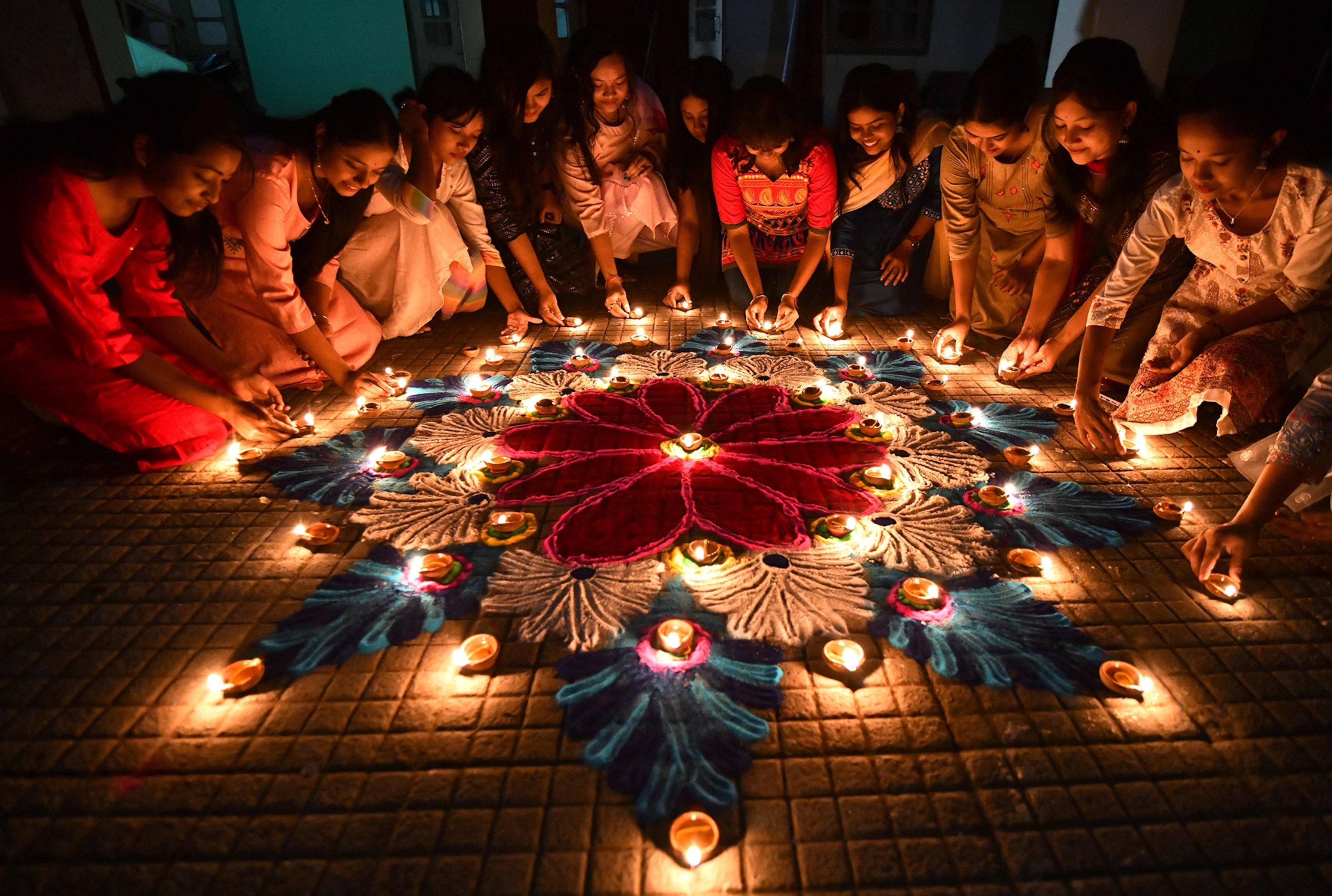 Students light earthen oil lamps on rangoli, a decorative design, on the occasion of the Diwali.