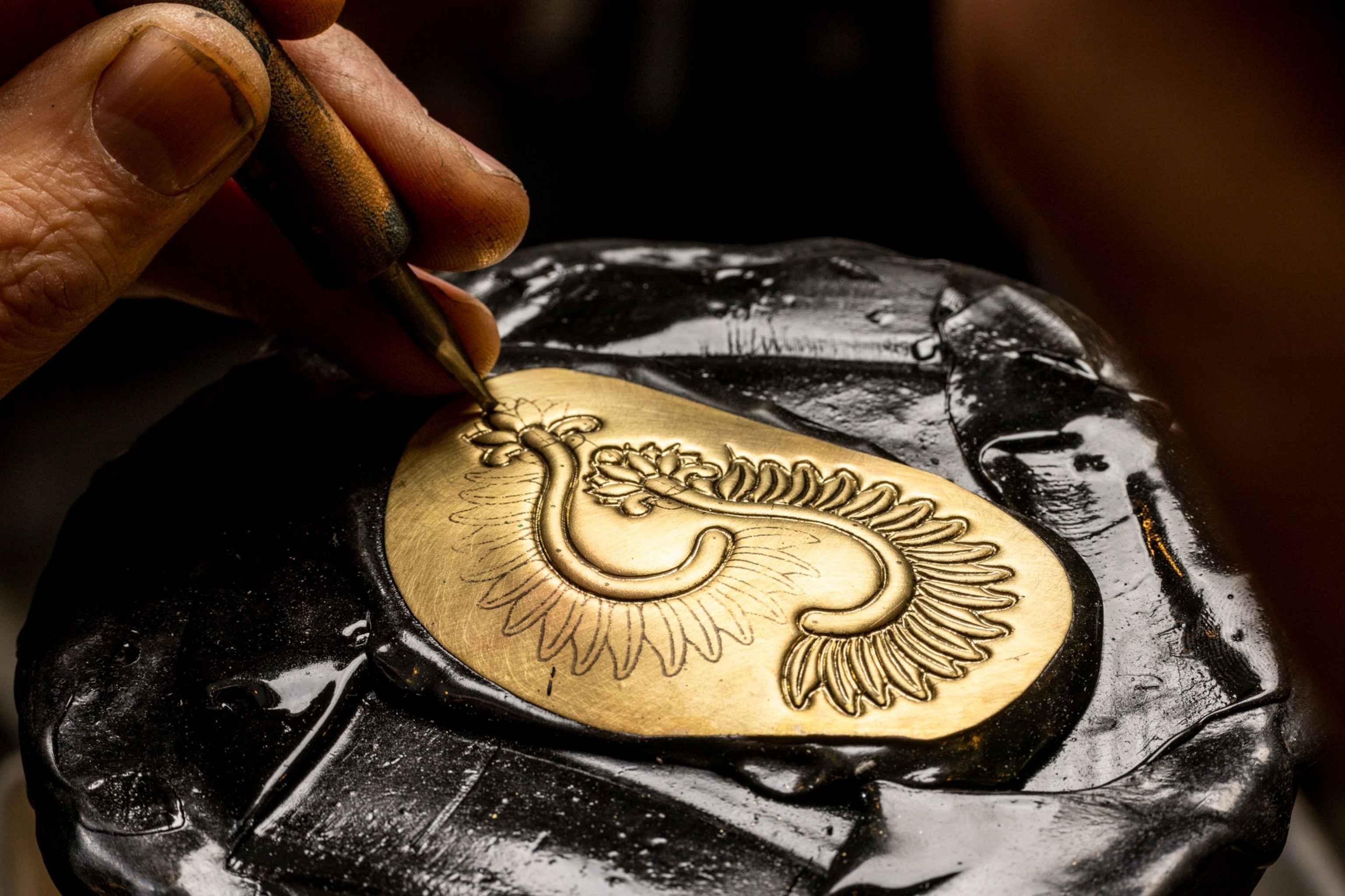 a man hammers a pattern into a piece of gold plate