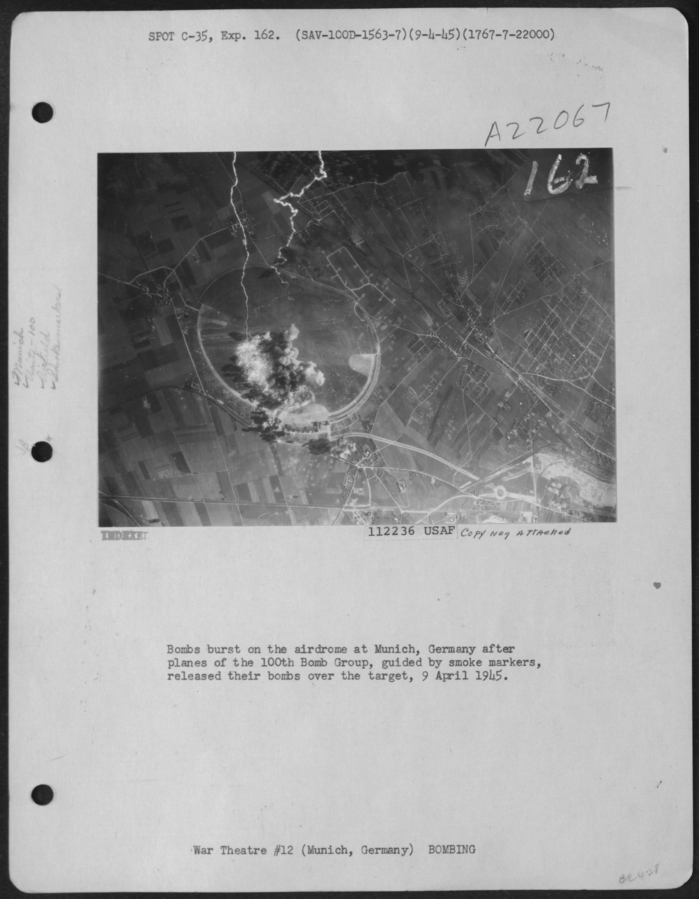 Black and white photograph of an aerial view of land, rivers, fields, and towns. with pillows of smoke rising up from part of the lower left corner of the photograph.