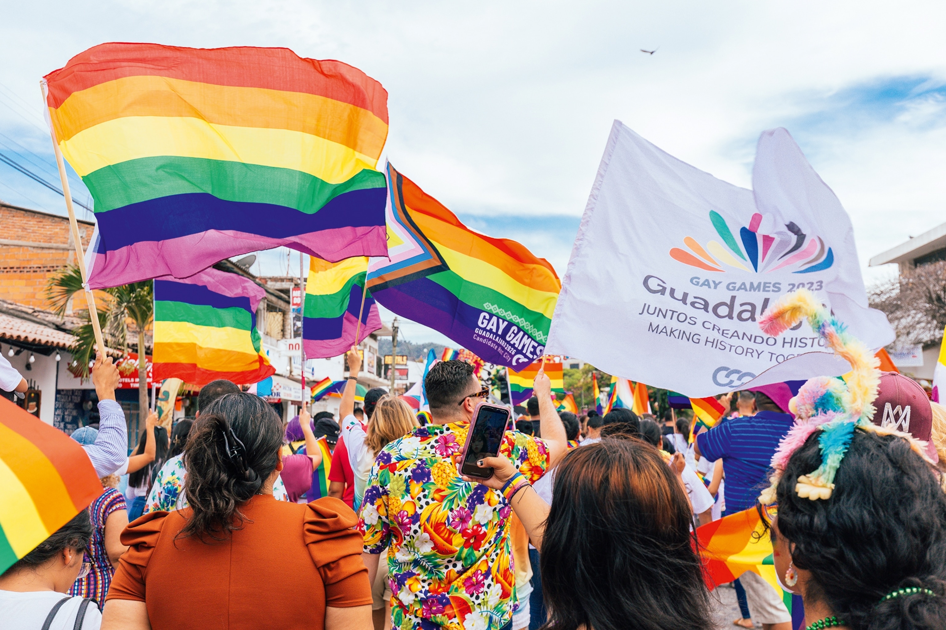 A gay pride parade in Sao Paulo. Attendees are waving the pride flag, all wearing bright coloured clothing.