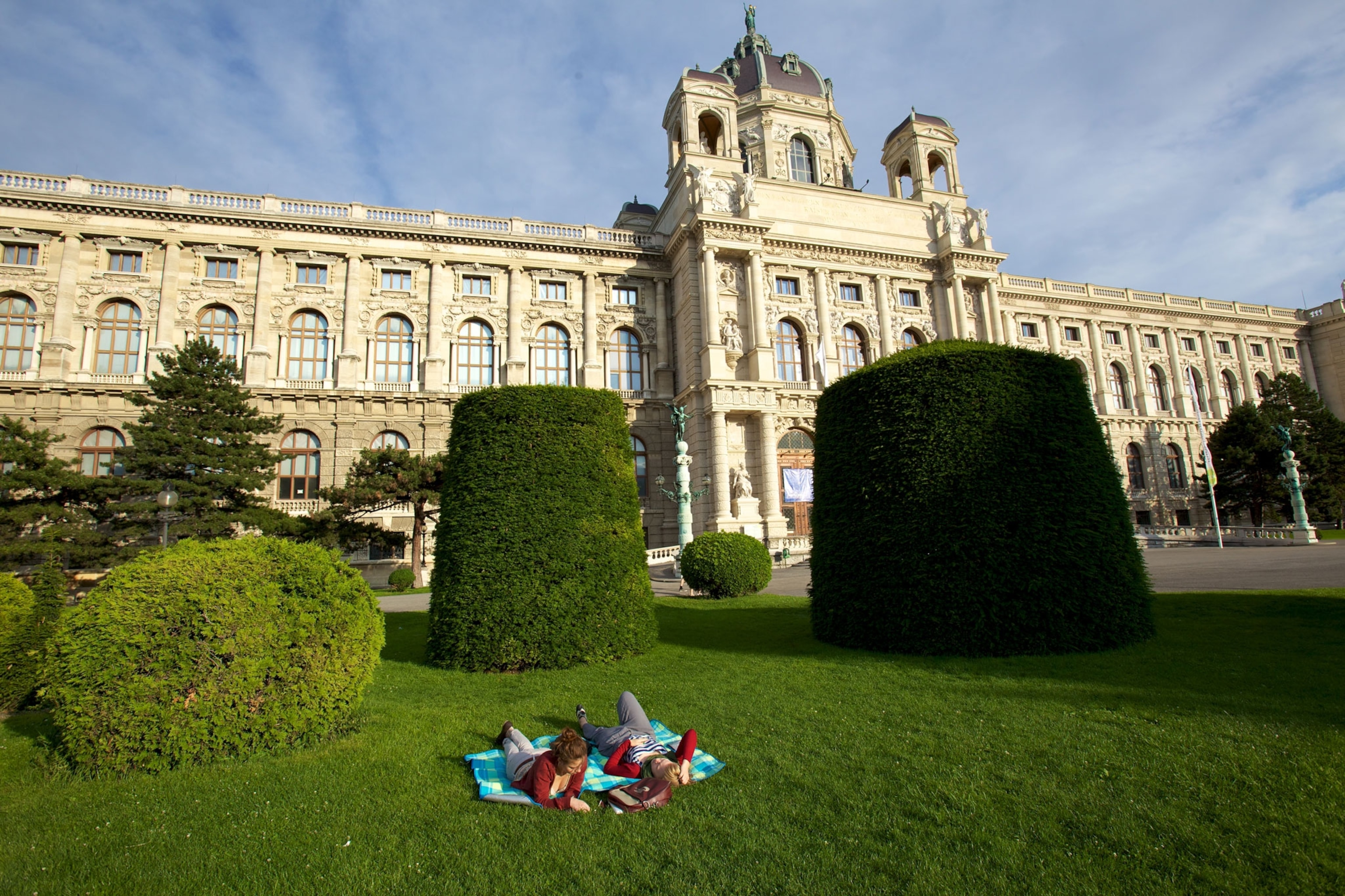 Two women relax on a lawn outside the Art History Museum.