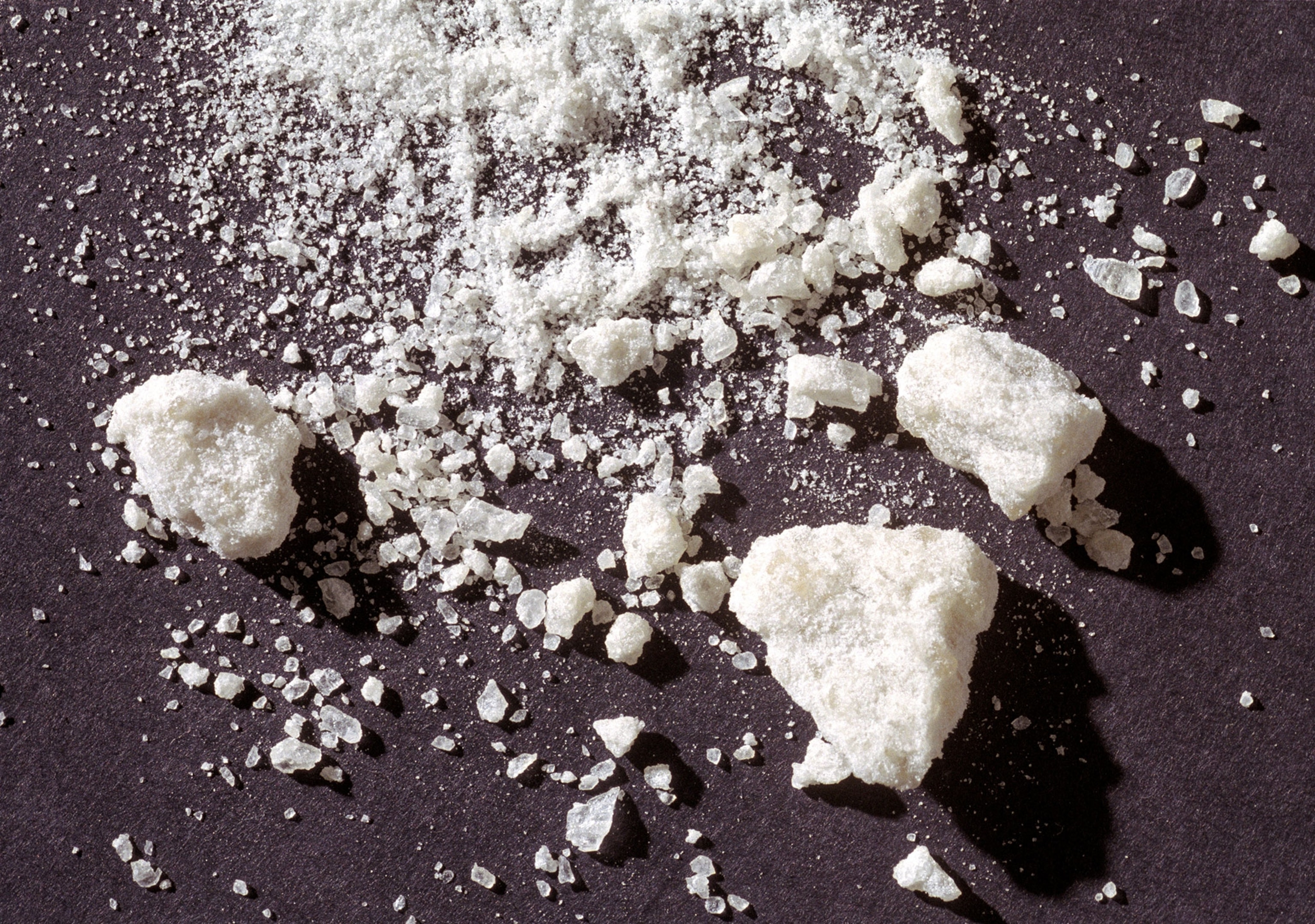 White, crumbly, rock like substance surrounded by smaller pieces of the substance and white powder on a black background.