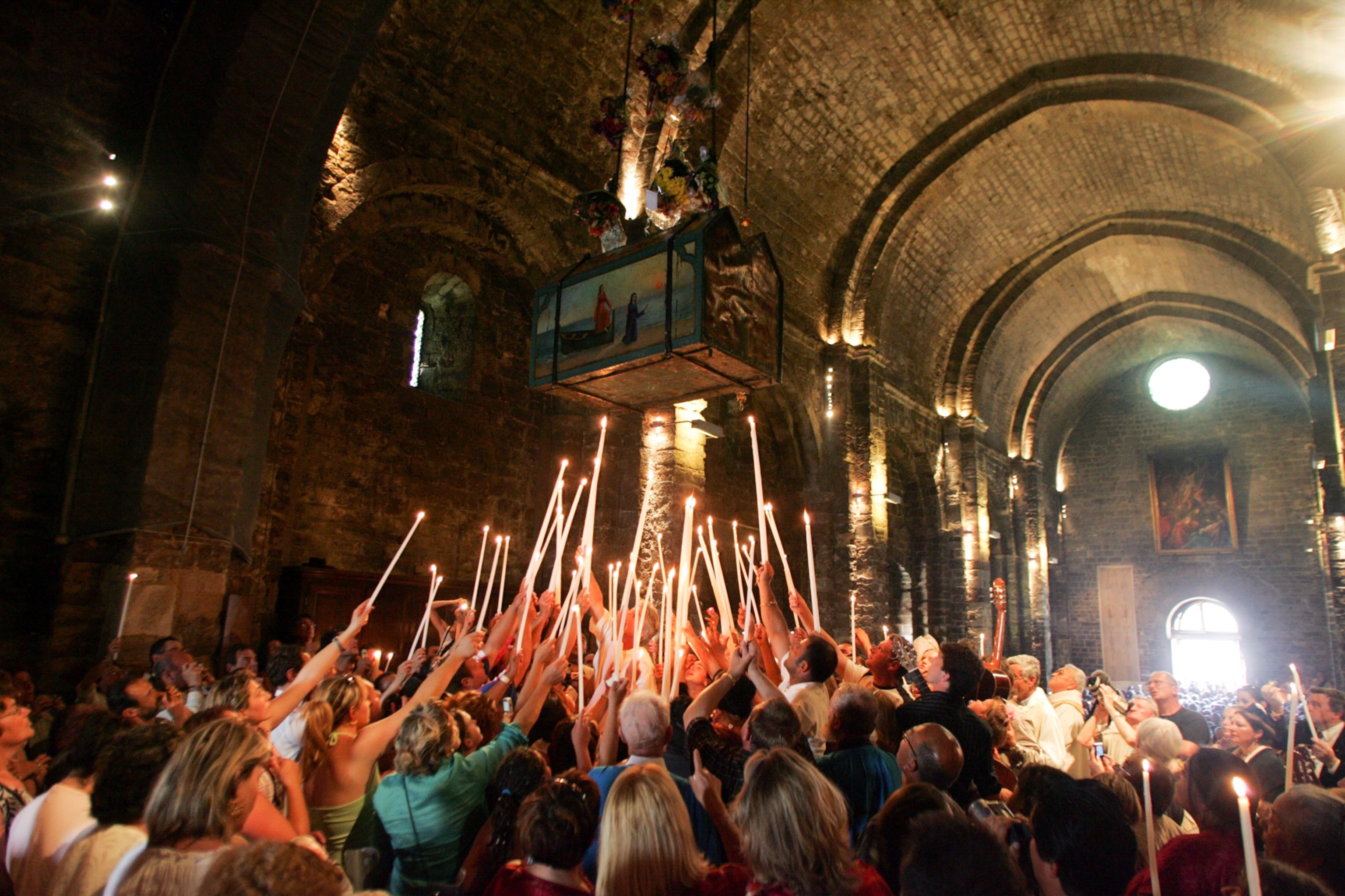 Worshipers inside the Church of Les Satines Maries de la Mer raise candles as relics of Black Sara are lowered in a painted chest.