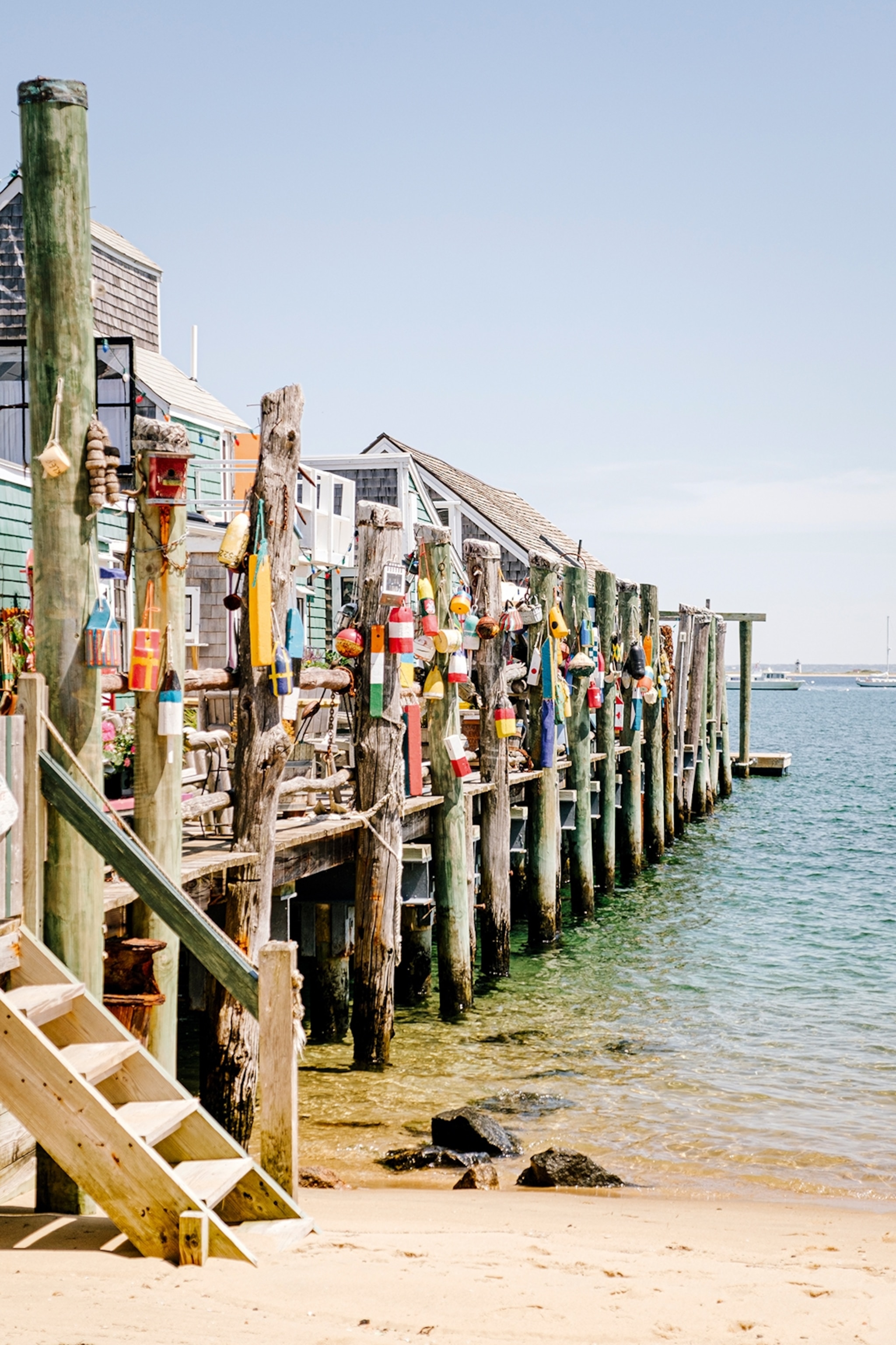 Beach with a dock extending out into the sea with colourful huts on the boardwalk