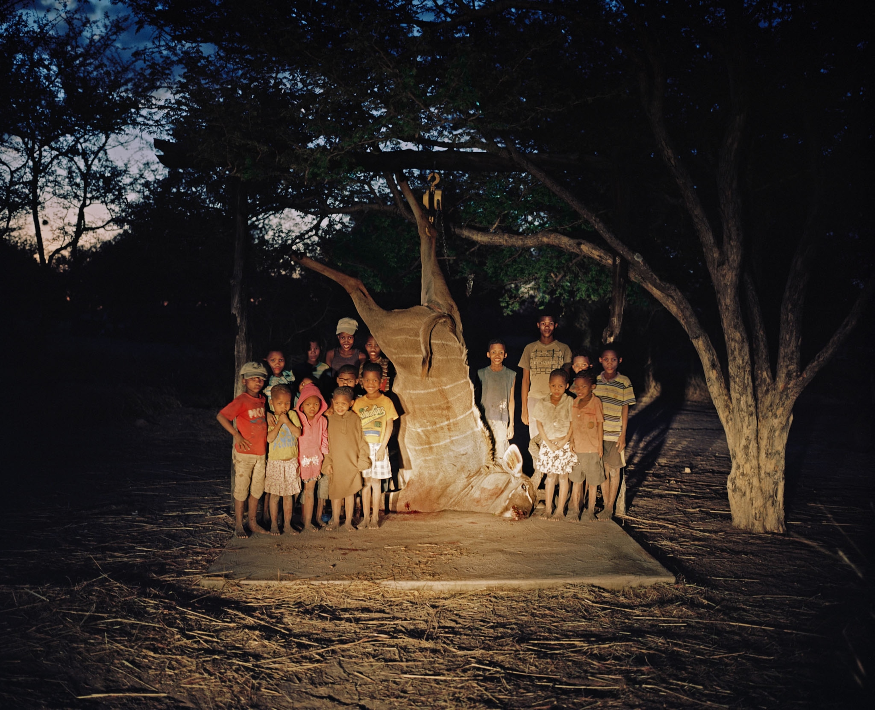 children posing with a dead animal tied to a tree at dusk