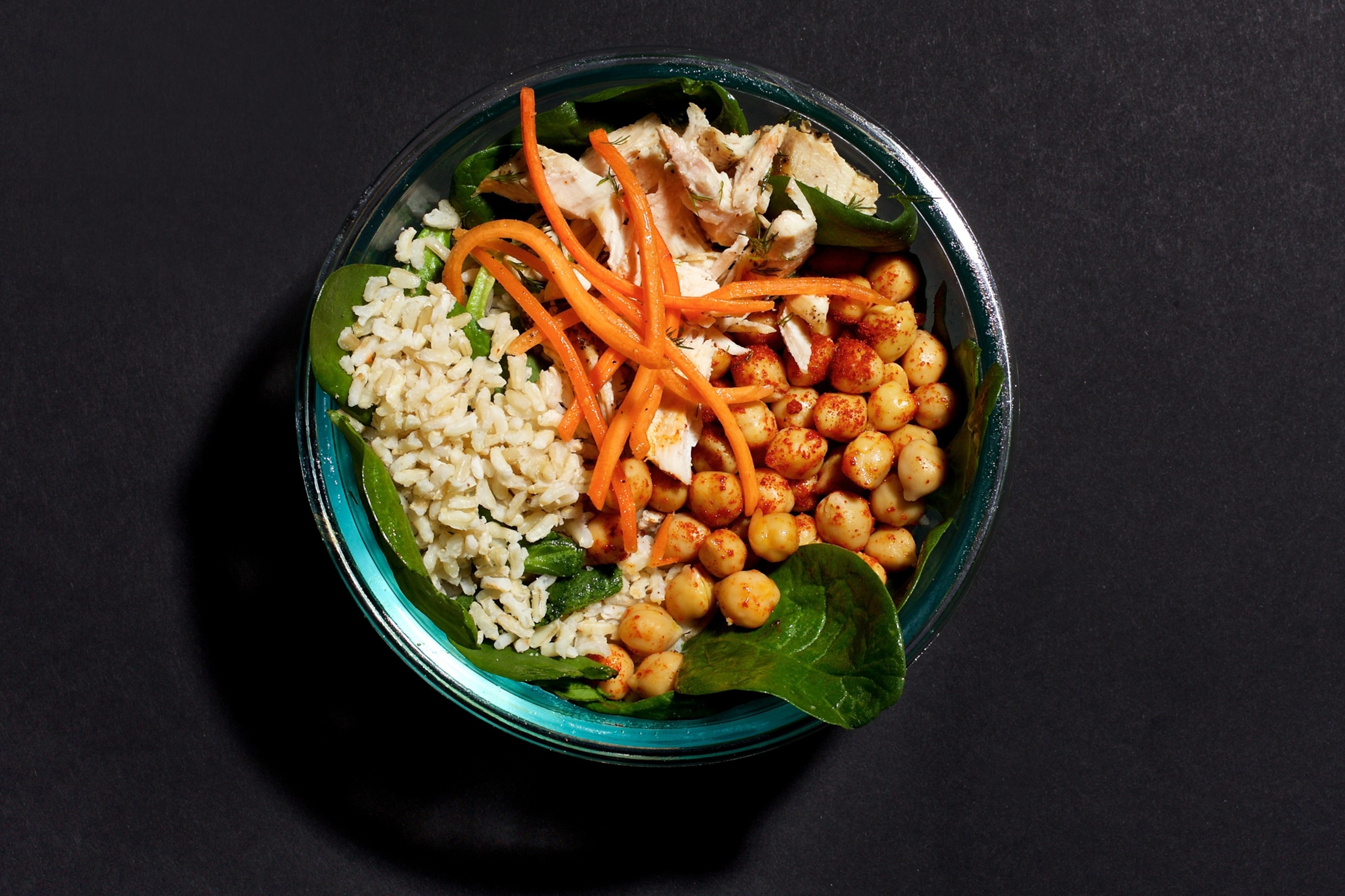 A bowl containing various sources of protein, including chicken, chickpeas, spinach, and whole grain rice.