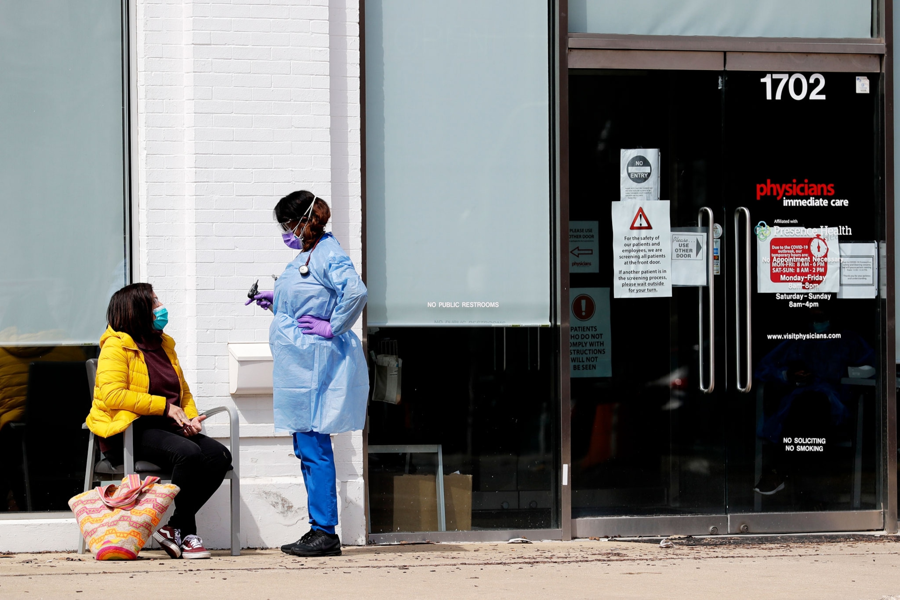 a woman in scrubs talking to a seated woman on a sidewalk