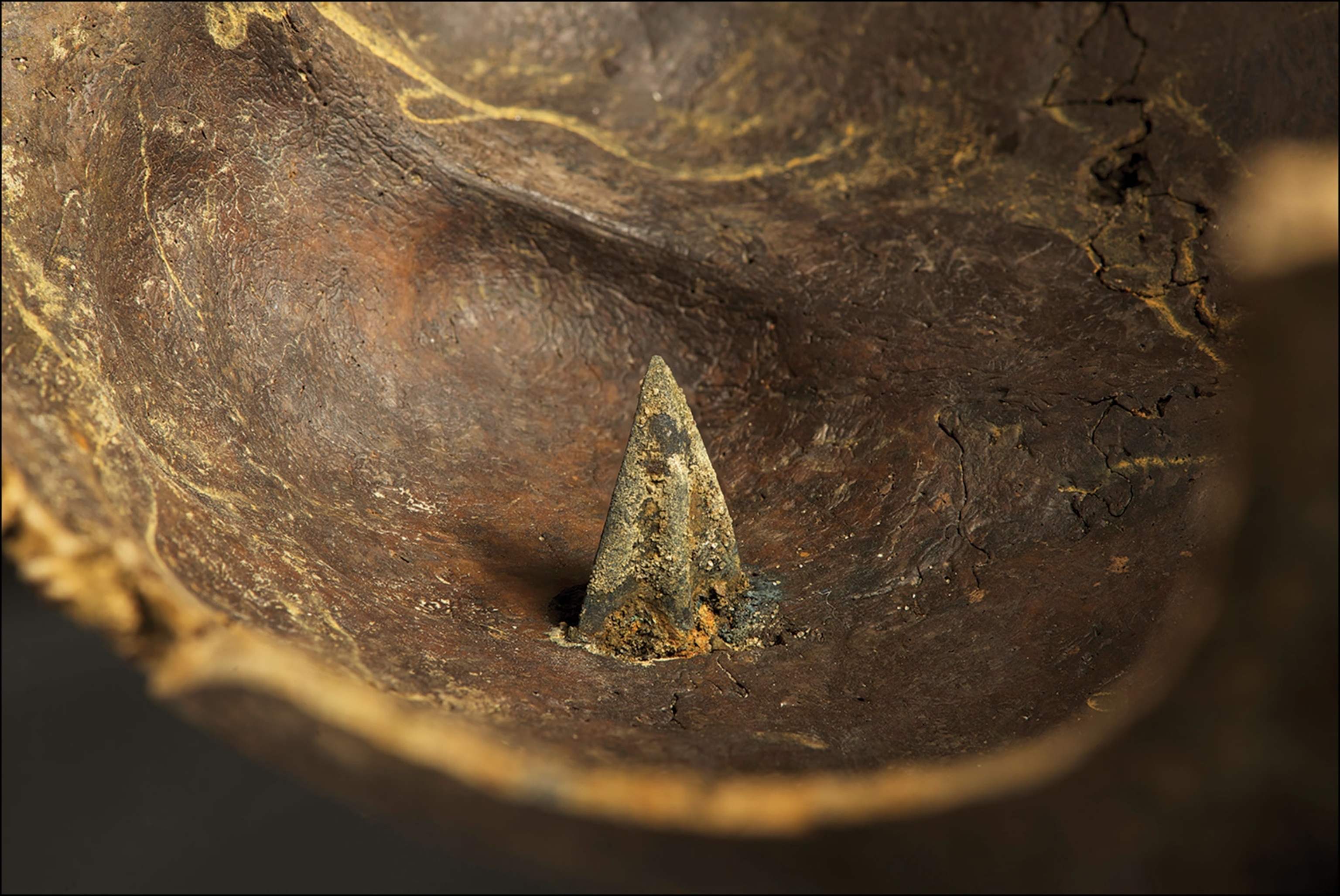 Arrowhead sticking out of a bronze helmet.