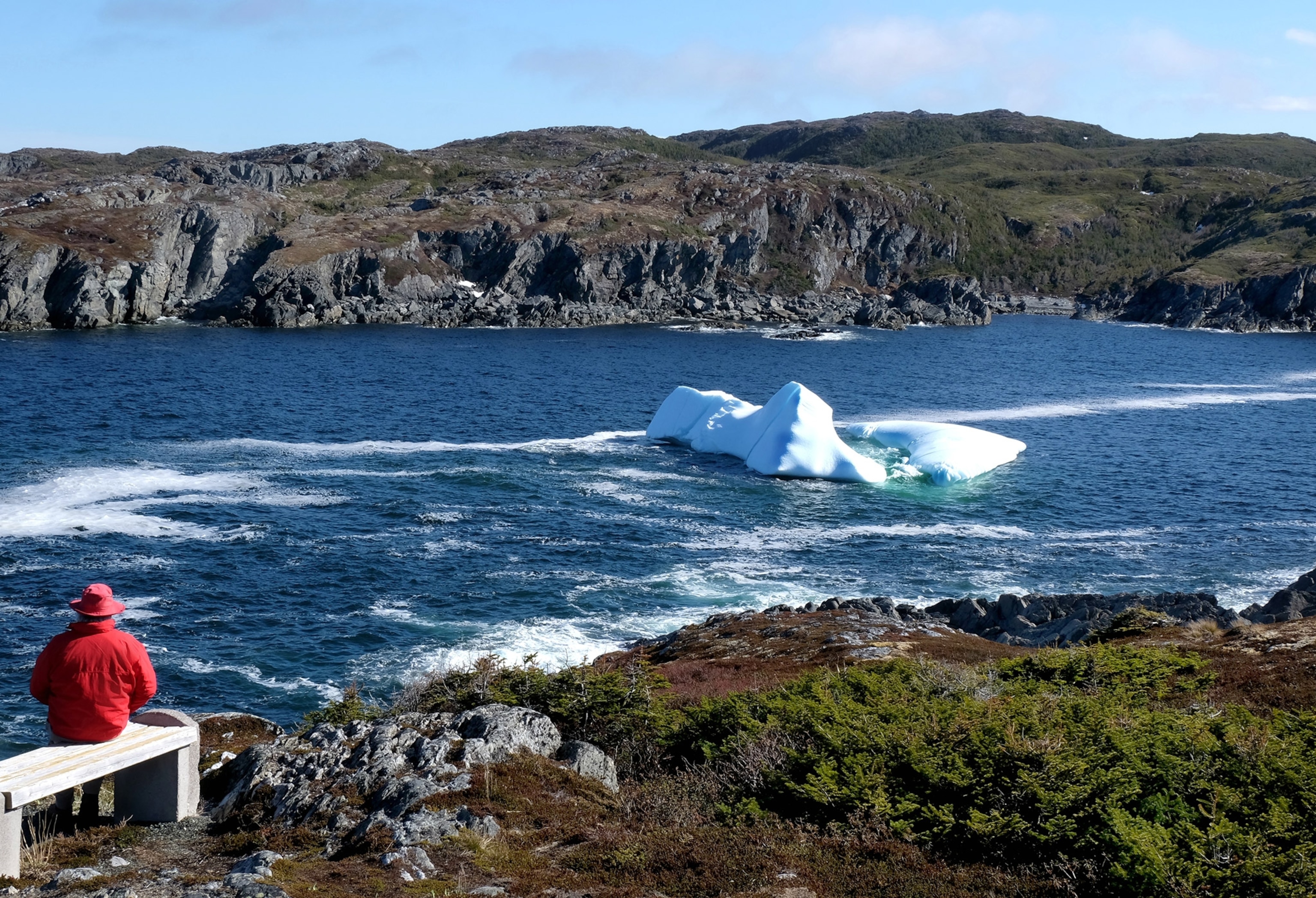A Person looks in the distance at an iceberg with red hat and jacket.