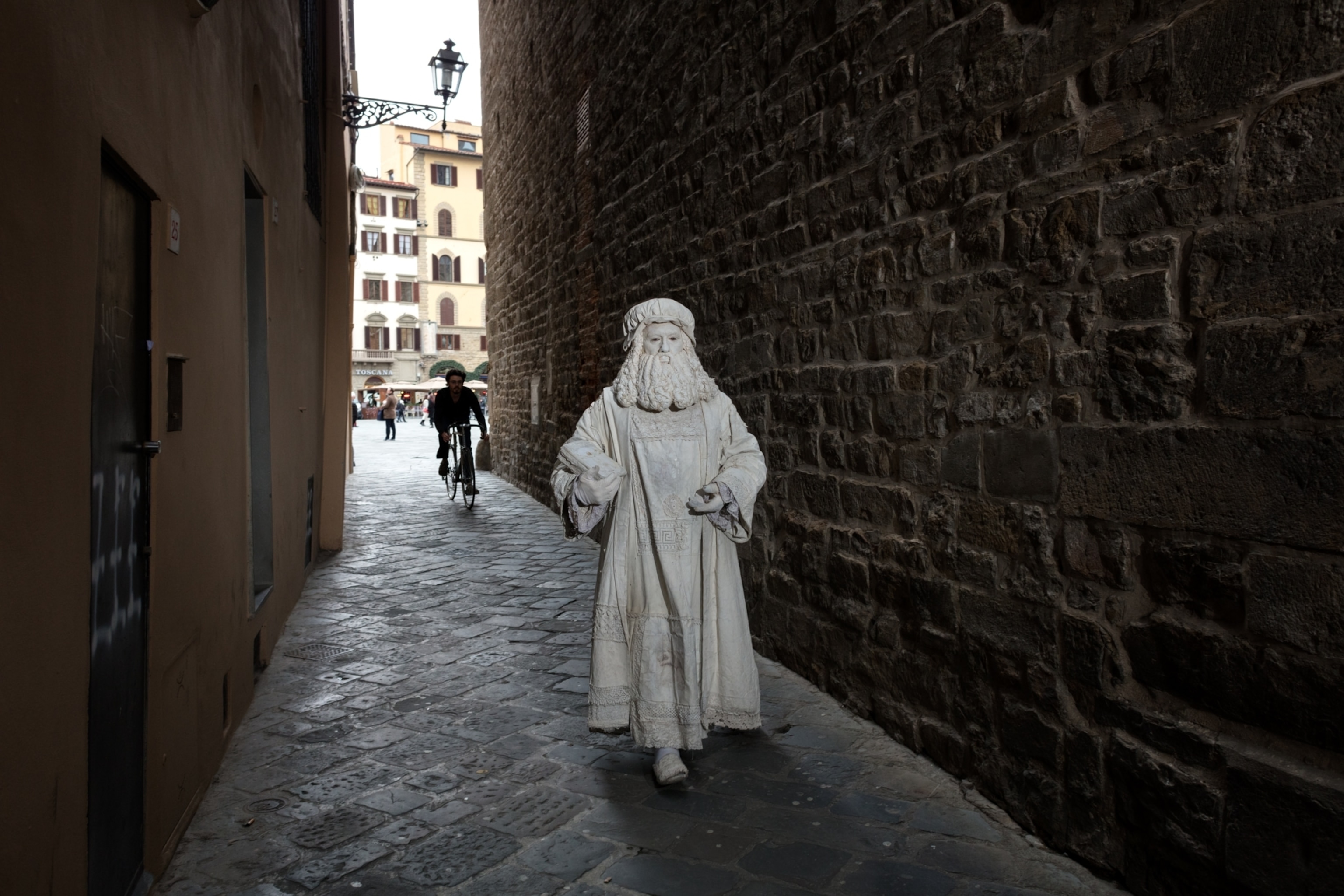 a man in an all white medieval costume and white face paint walking in an alley