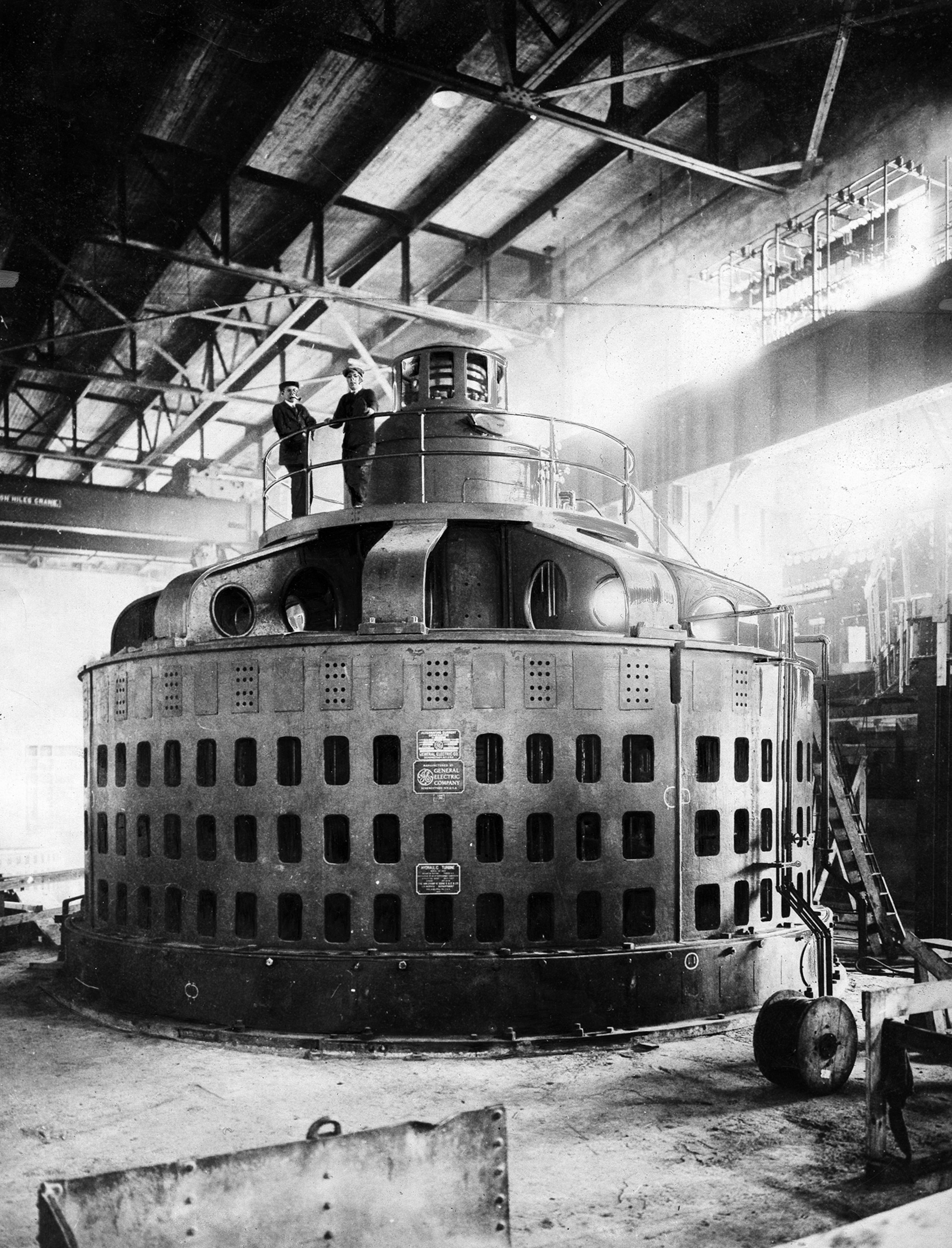 A black and white image of two men standing on a large metal device.