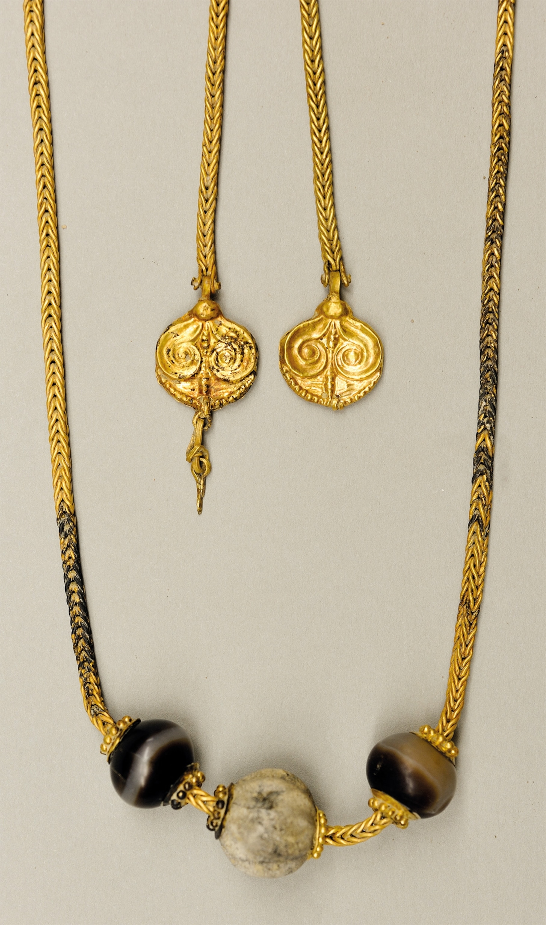 A woven golden necklace reflects styles found in Crete and in the Peloponnese region, the heartland of Mycenaean culture. It is adorned with beads, two of agate and one of faience, and two gold finials.