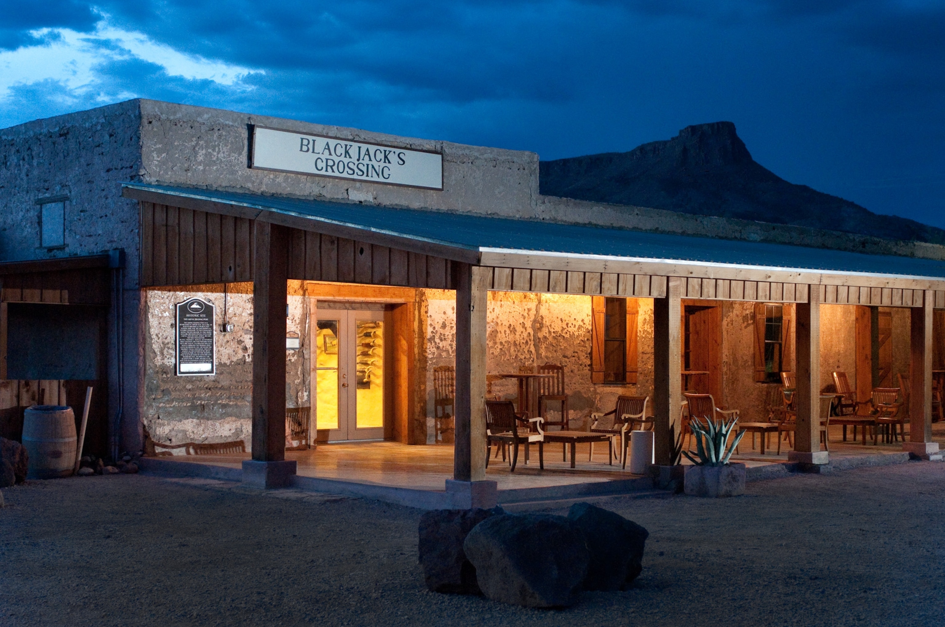 A building at dusk with a patio lit up. Dark blue night sky above and mountains in the distance.