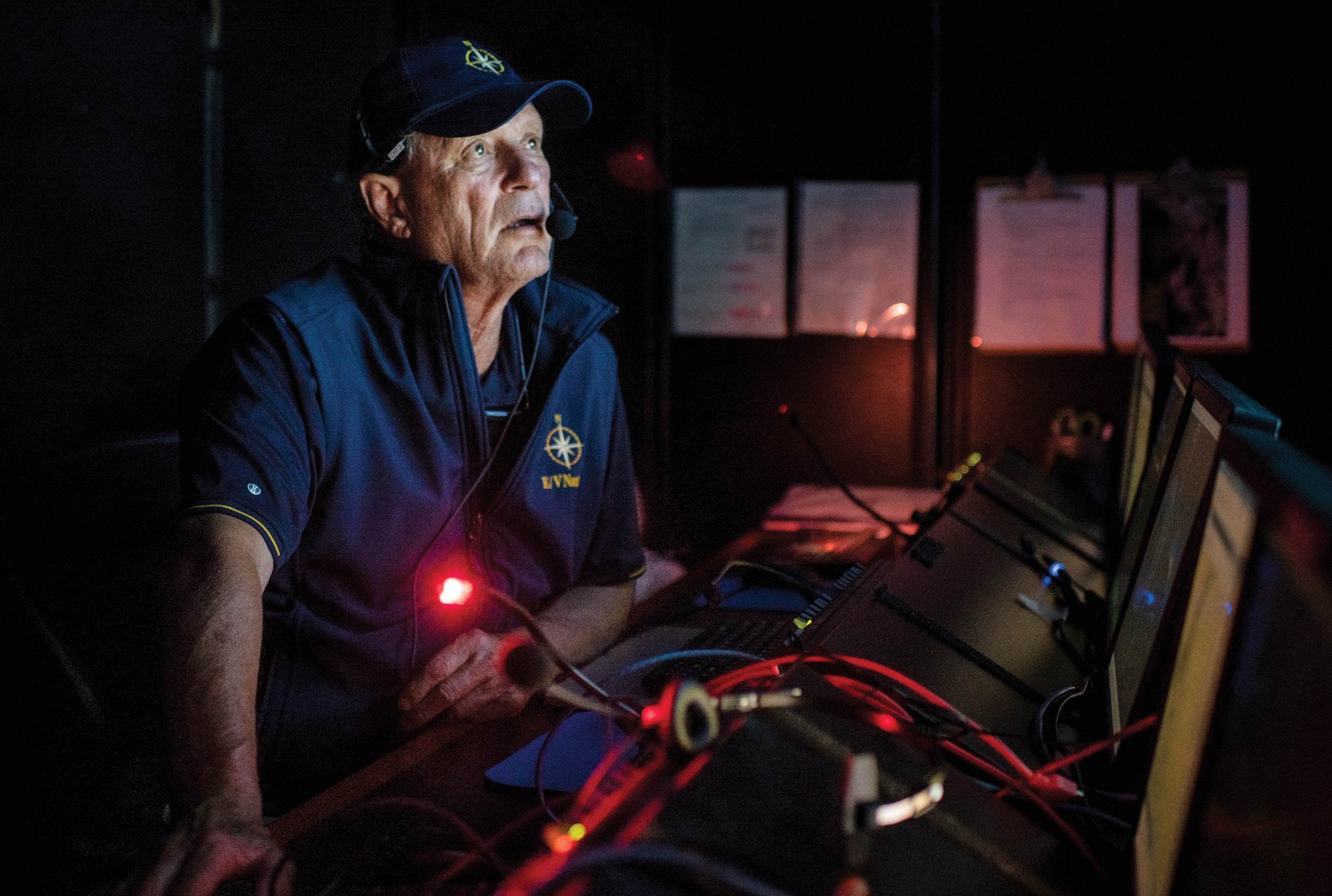 A close up image of Bob Ballard with a hat and under red lights staring intently.