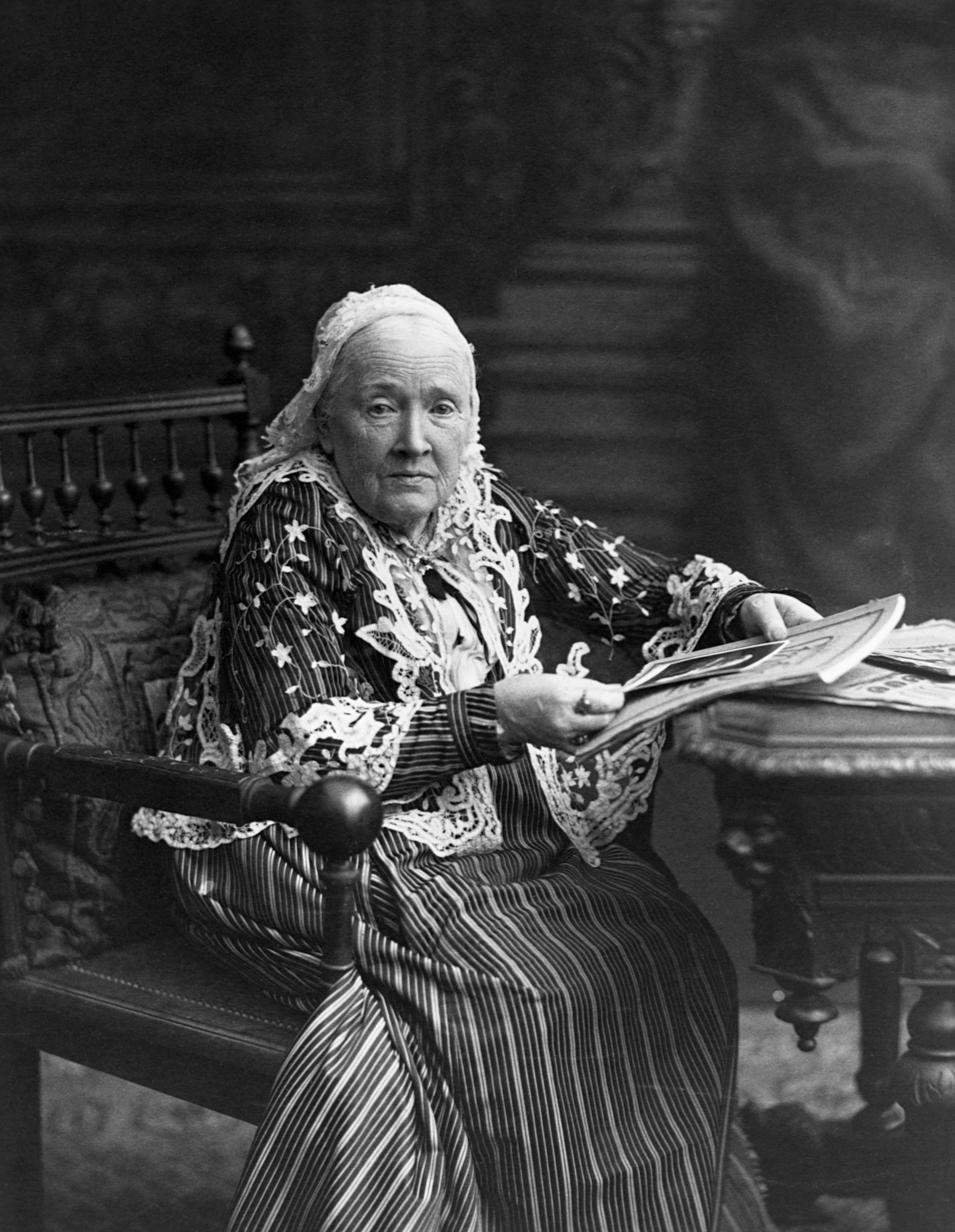 a black and white portrait of an older woman sitting at a table wearing a bonnet
