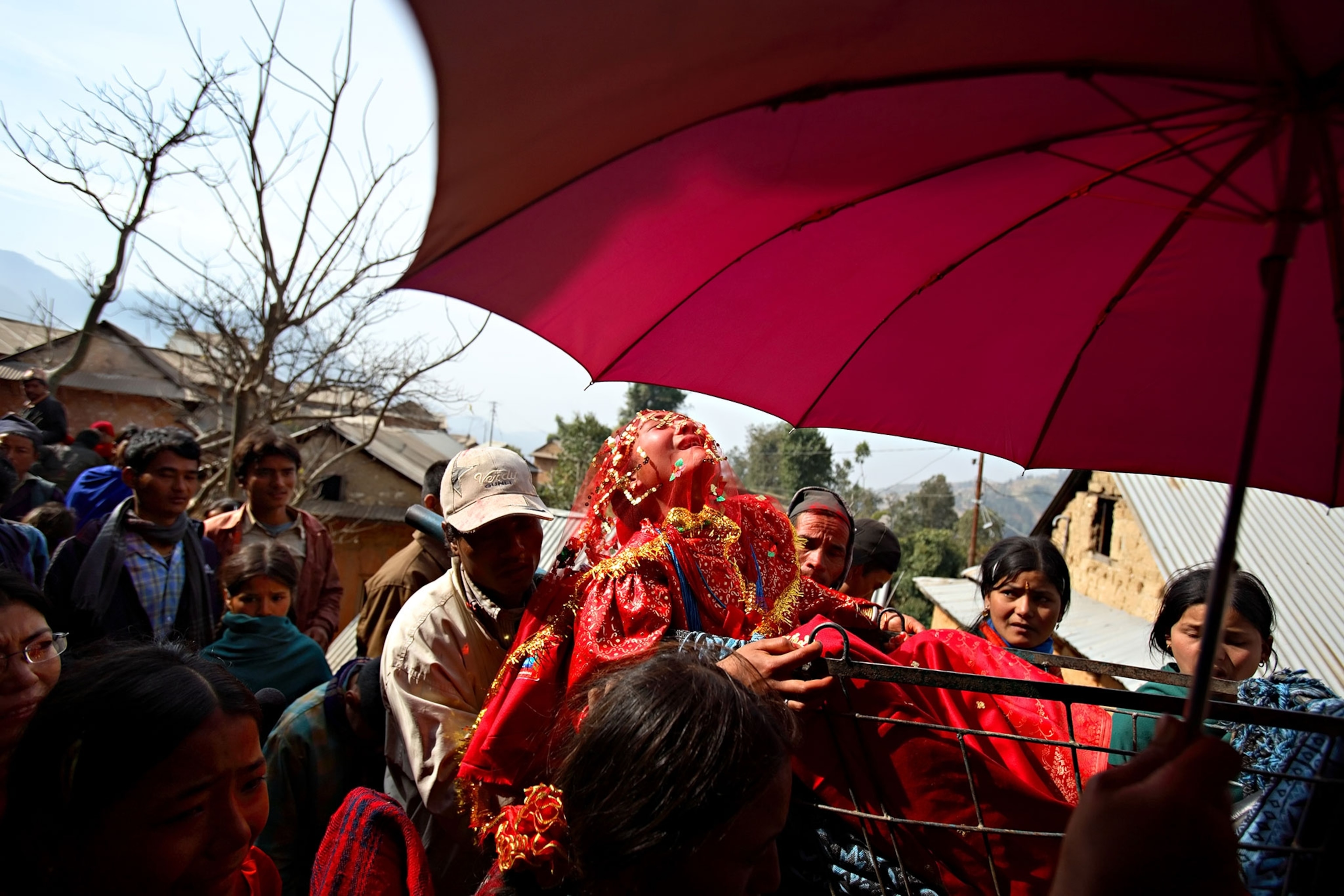 A girl with a red veil covering her face screams out as she is carried to the home of her new husband in Kagati, Nepal