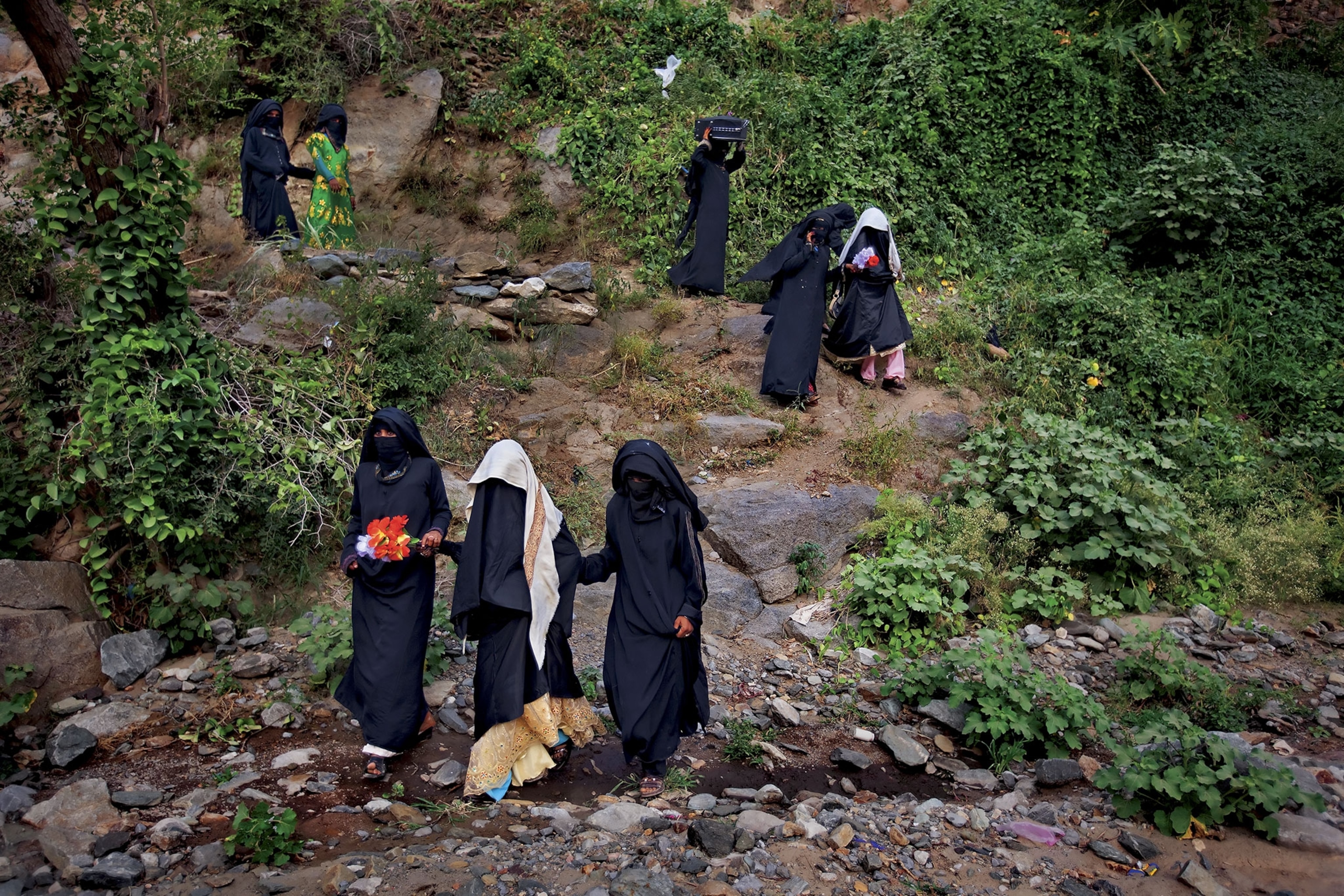 young brides veiled in black walk down a hill after a wedding party with female relatives, escorted to a new life with their husbands