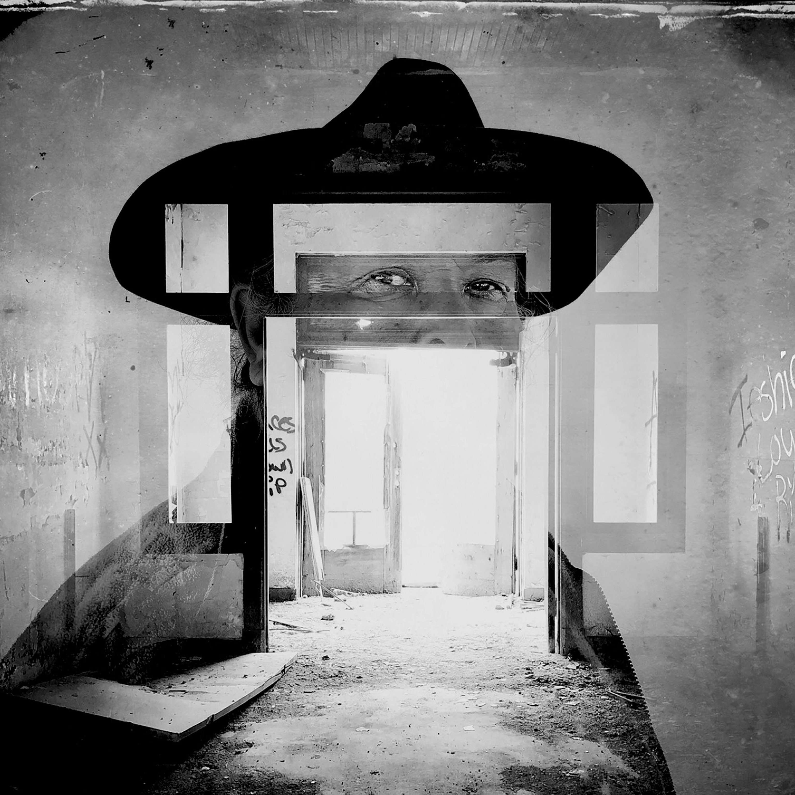 Picture of b&w portrait of man in whid-brim hat and abandoned room with open door seen through him.