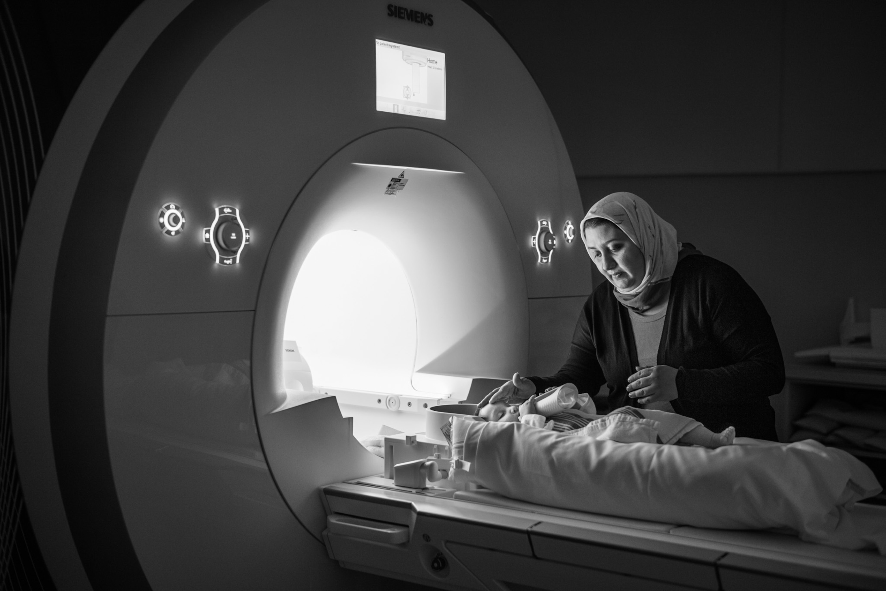 a woman looking over her daughter lying in a bed next to a brain scanner opening