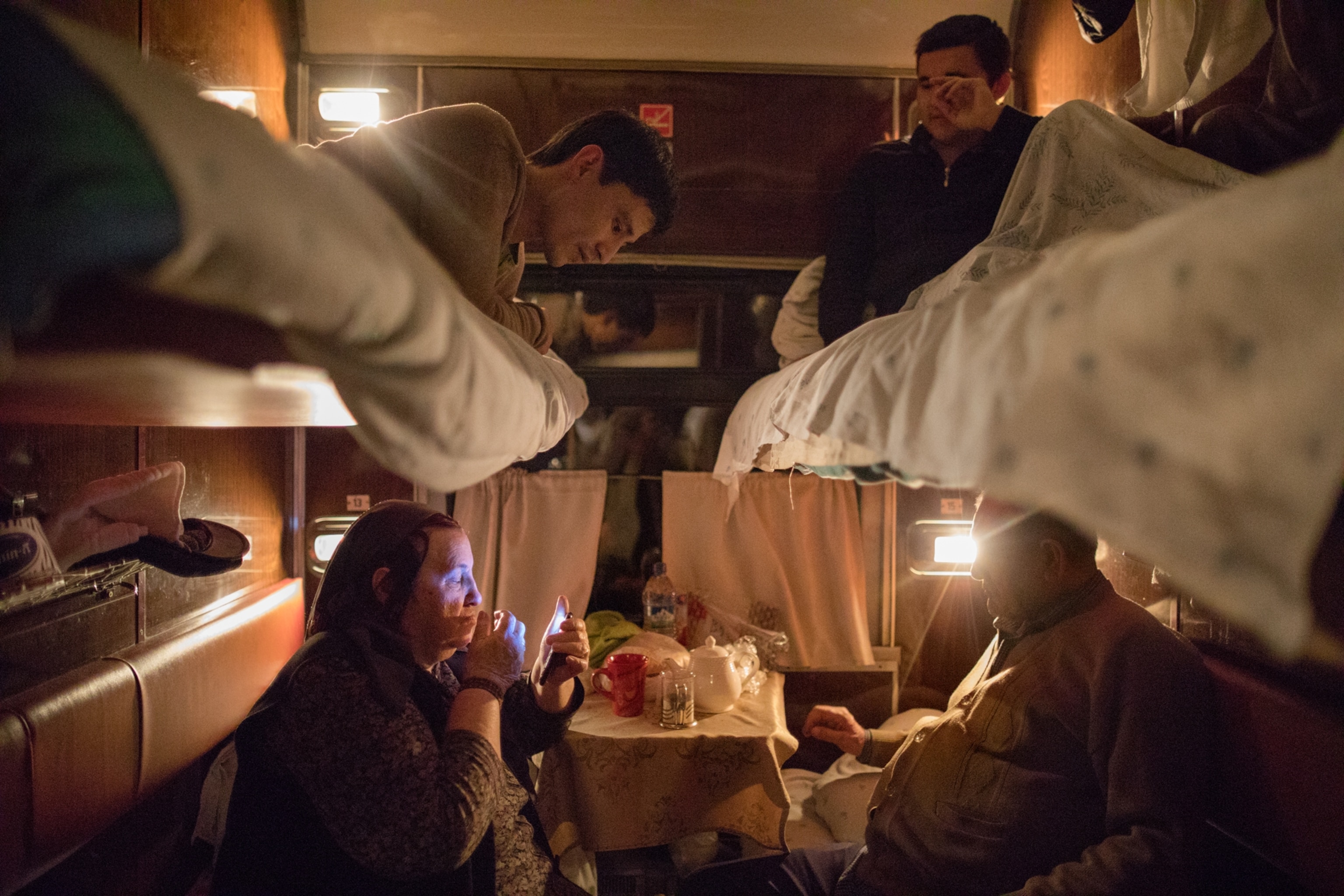 grandsons lying in beds above their grandmothers on a candle-lit train