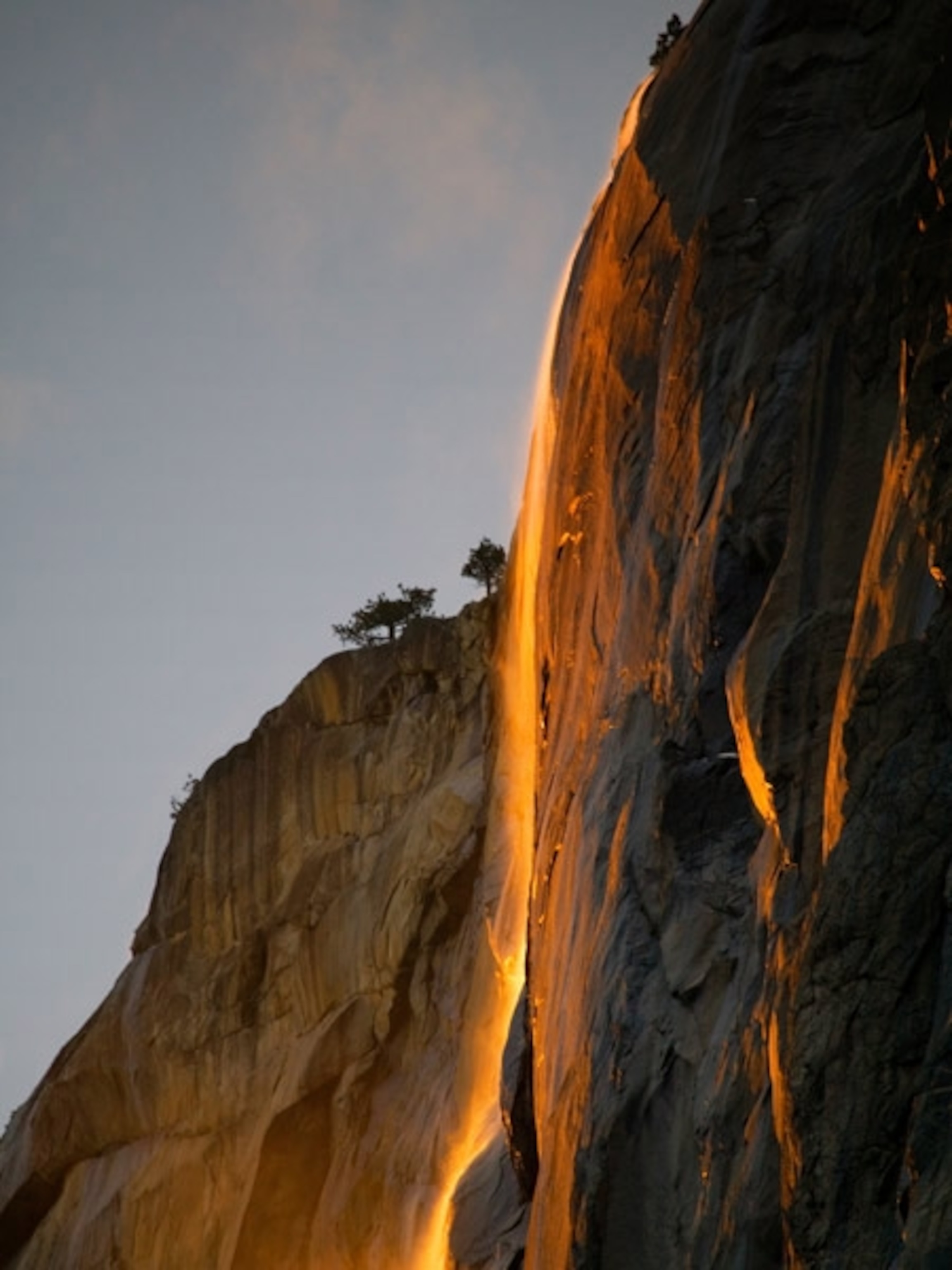 Glowing waterfall streams off large red cliff