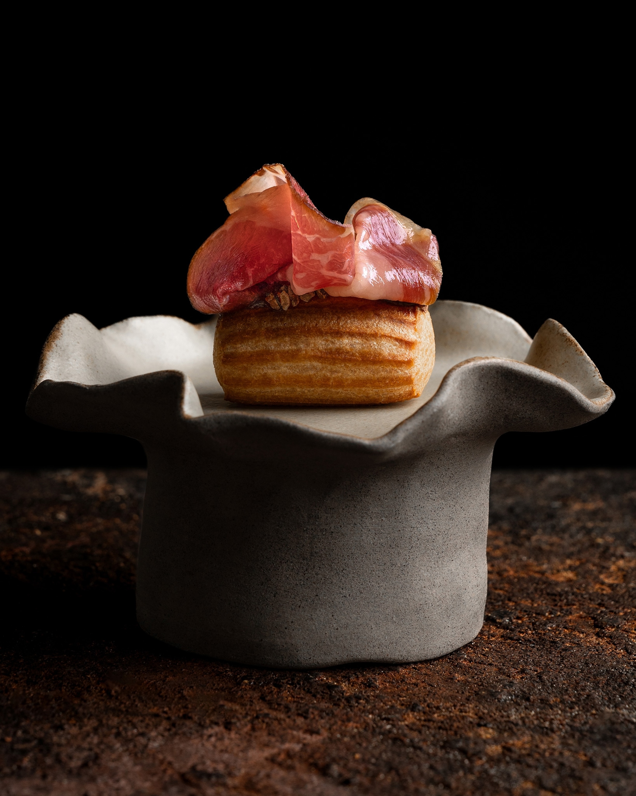 Orfali Bros's Umami Eclair with porcini emulsion & marmite, fermented quince glaze, cacao nibs, and beef prosciutto elevated on an elaborate stone dish.