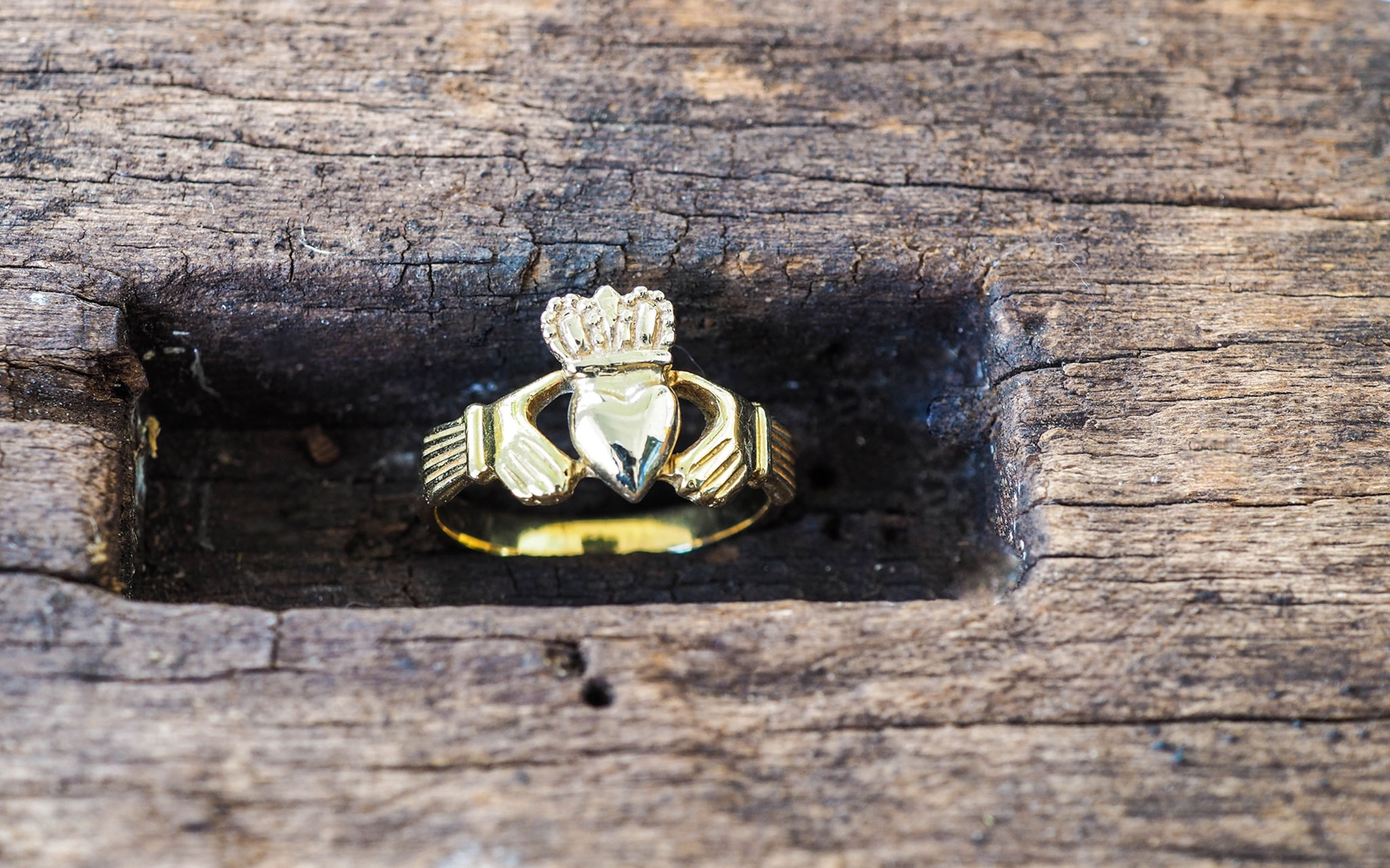 A gold, Irish ring with the symbol of true love with a heart shape and crown have two hand holding around the heart with wooden background.