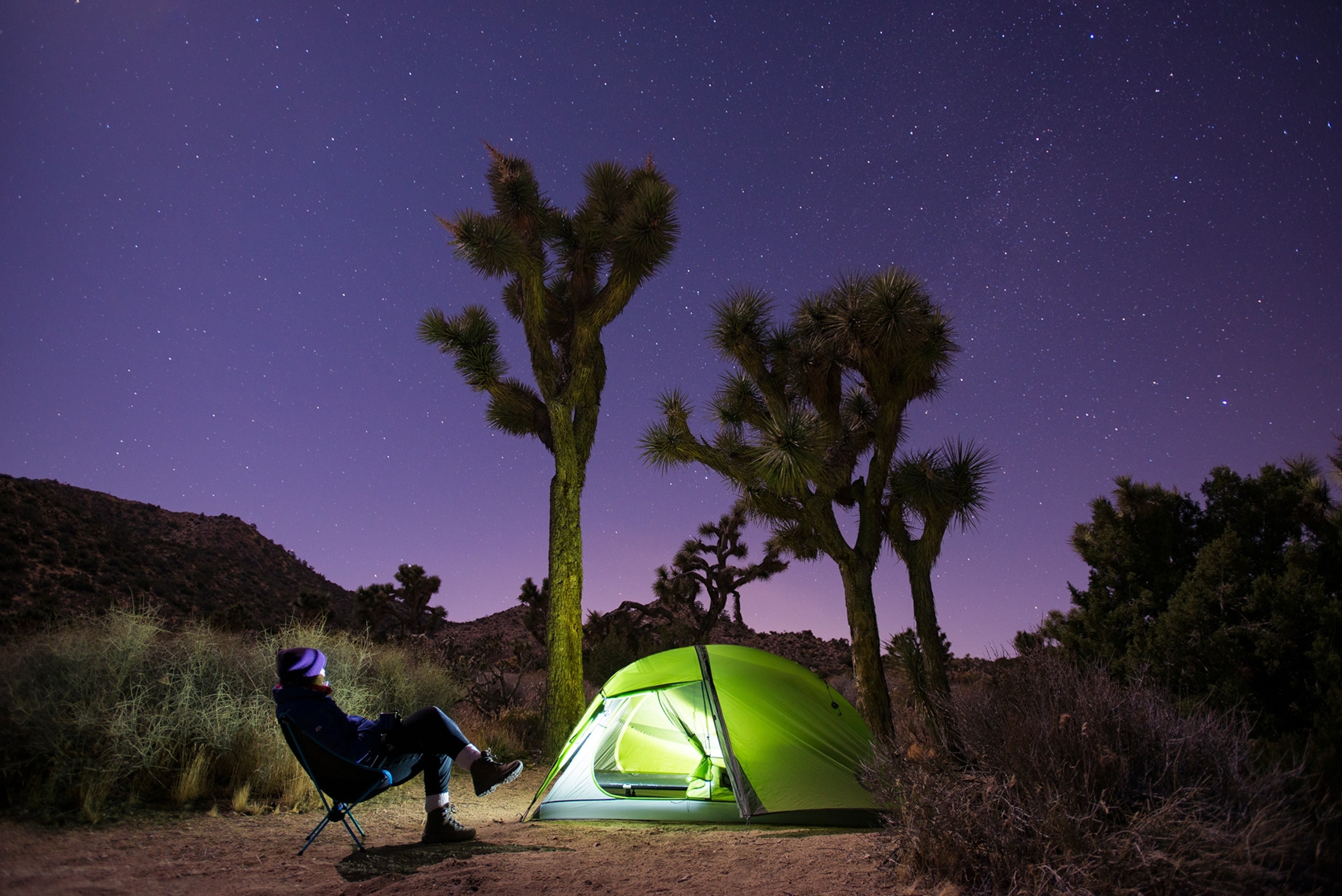 A man sits on a chair light illuminating their tent.