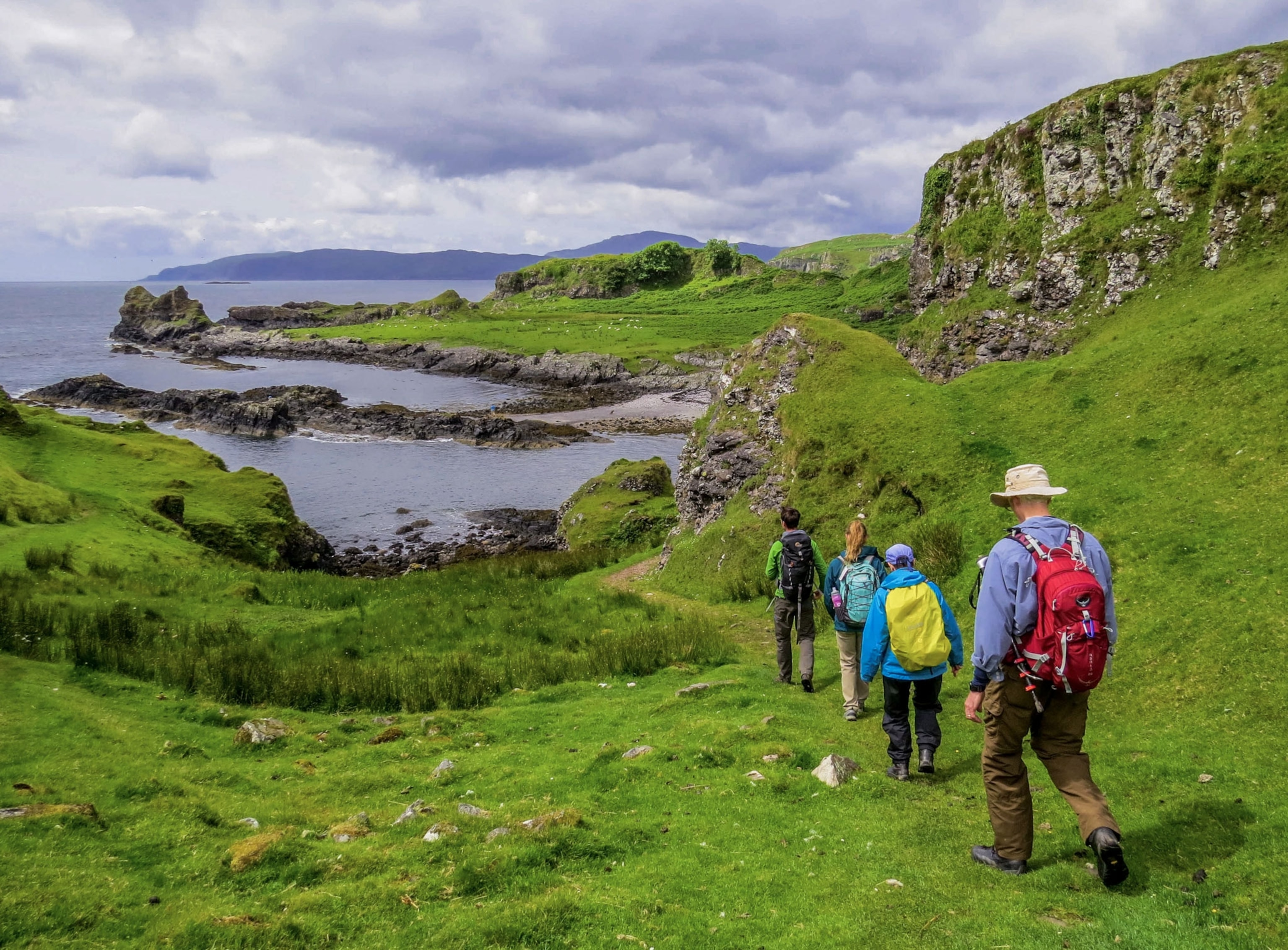 four hikers walk toward a body of water in a lush green landscape in Scotland