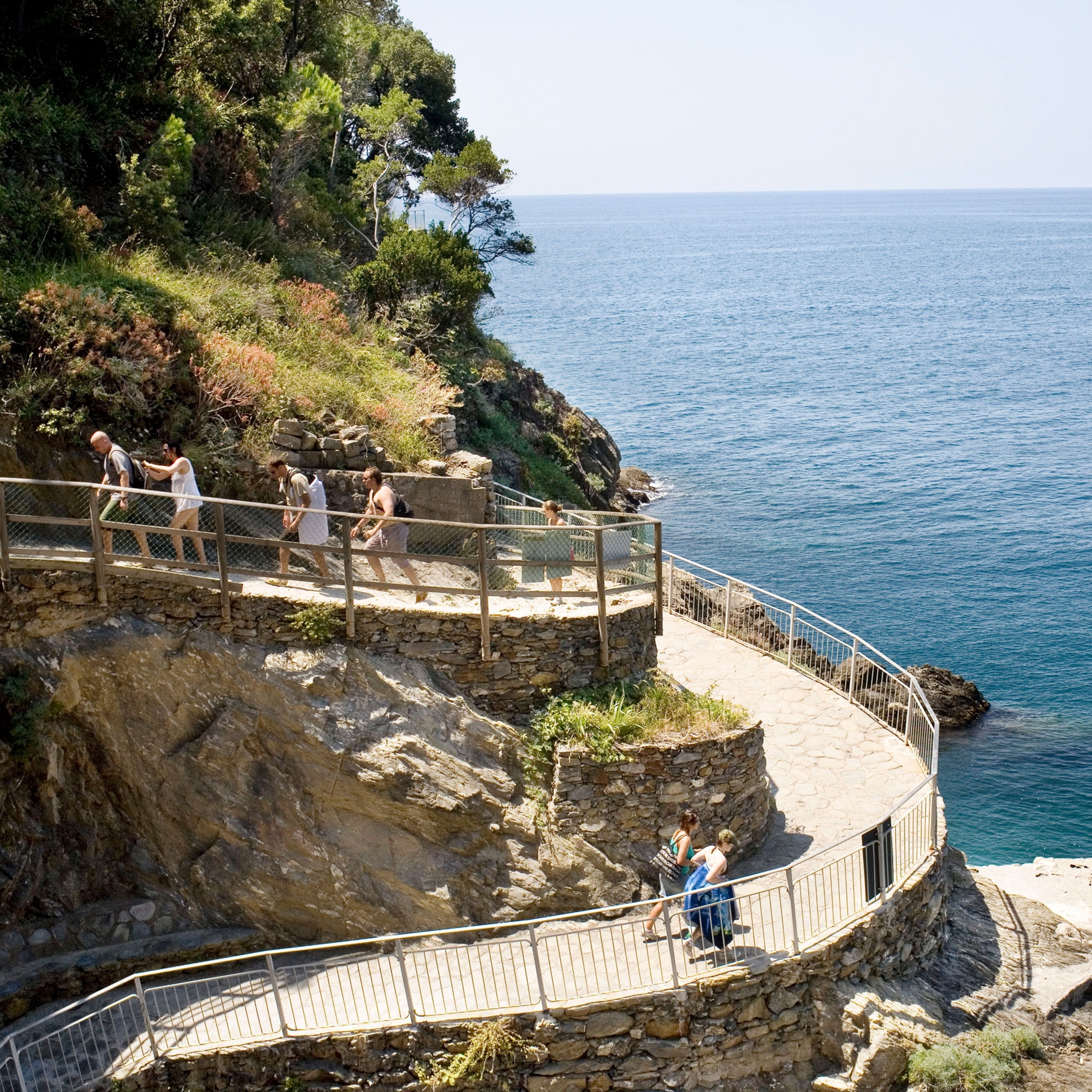 people walk up a winding path on a cliffside