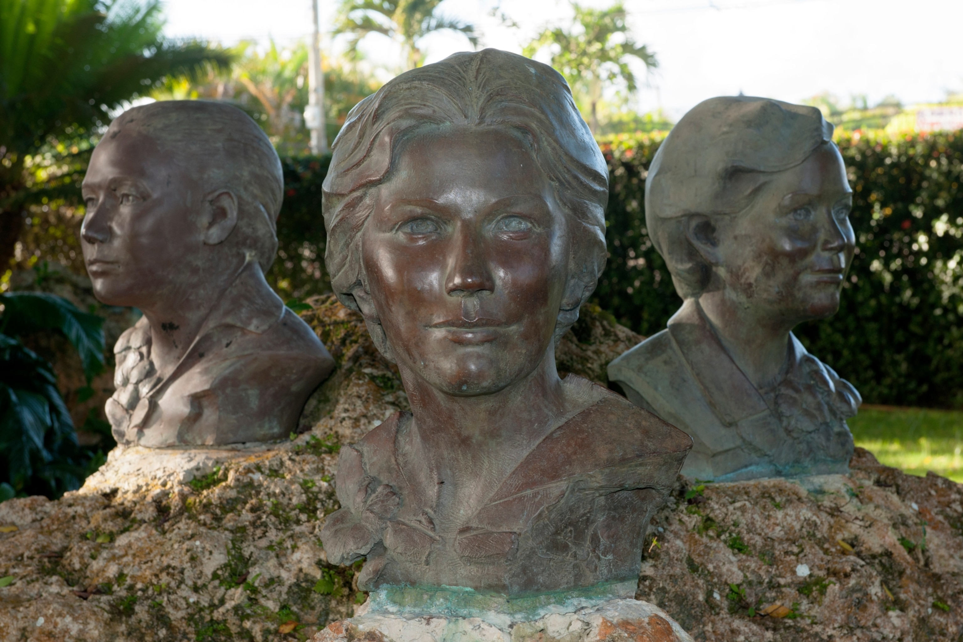 Three bronze busts of women amongst a garden.