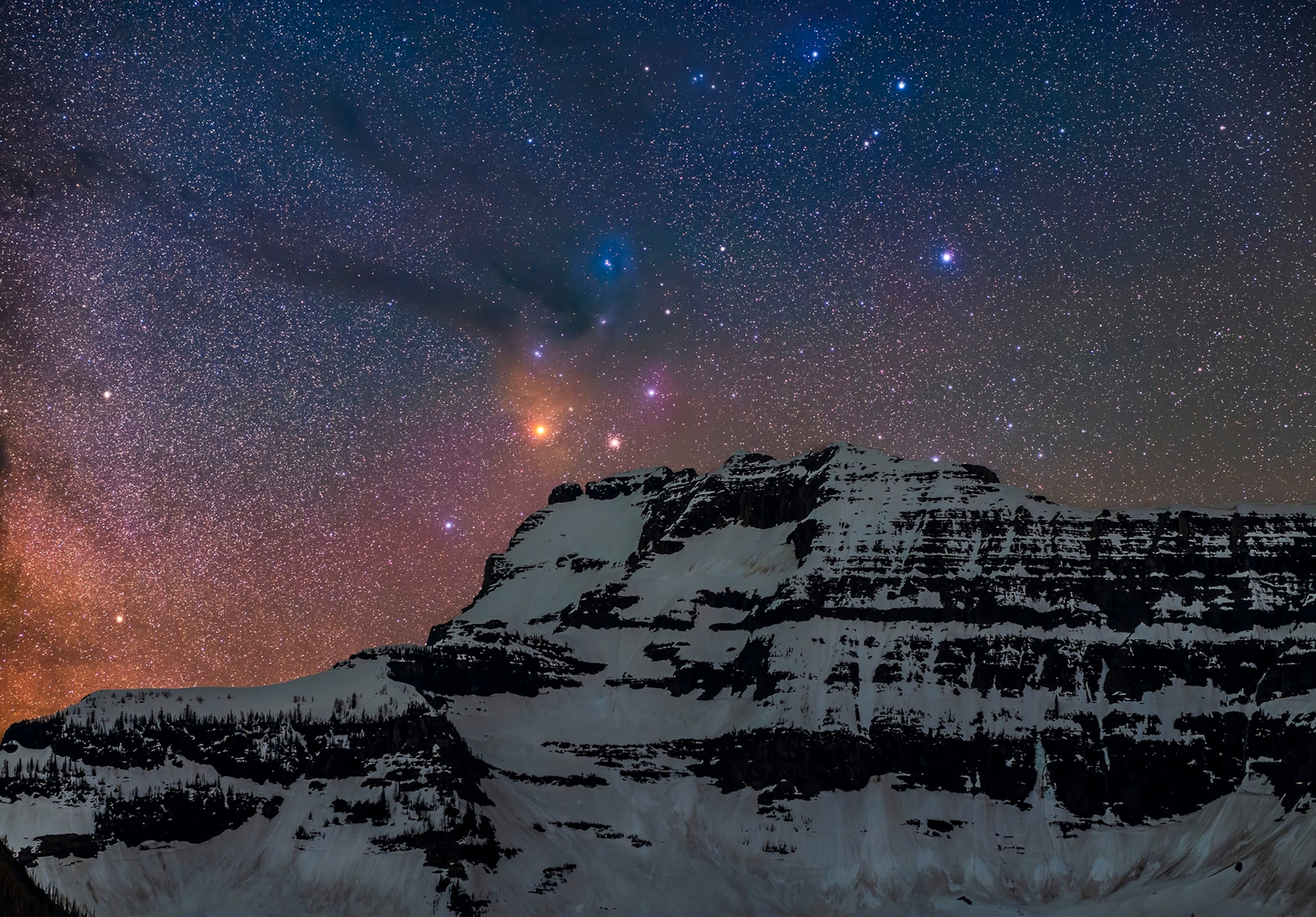 A "deepscape" image of the head of Scorpius with the colourful Rho Ophiuchi nebula complex culminating over the icy peak of Mount Custer in Montana, as taken from the north shore of Cameron Lake in Waterton Lakes National Park in Alberta, Canada. Antares is the yellow star, with the globular cluster Messier 4 just to the right. The mountain is lit only by starlight. This is from latitude 49° N so this area of sky is low in the south and just clears this mountain even with Scorpius at its highest, which it was here.