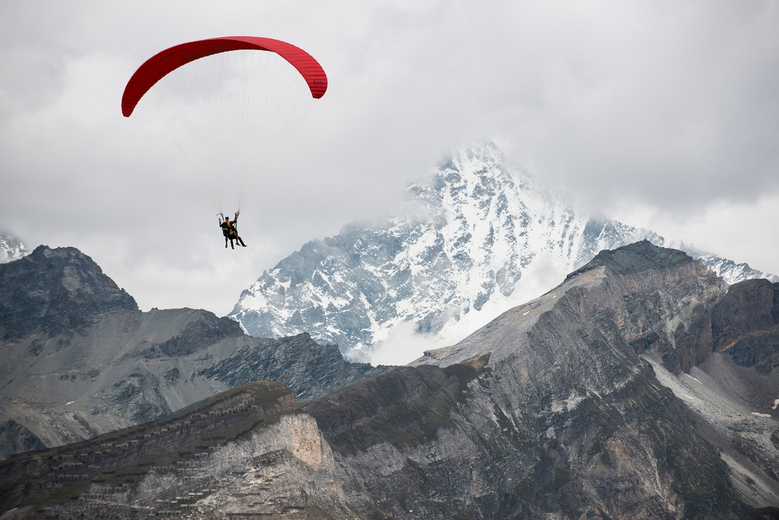 Person flying red paraglider over mountain.