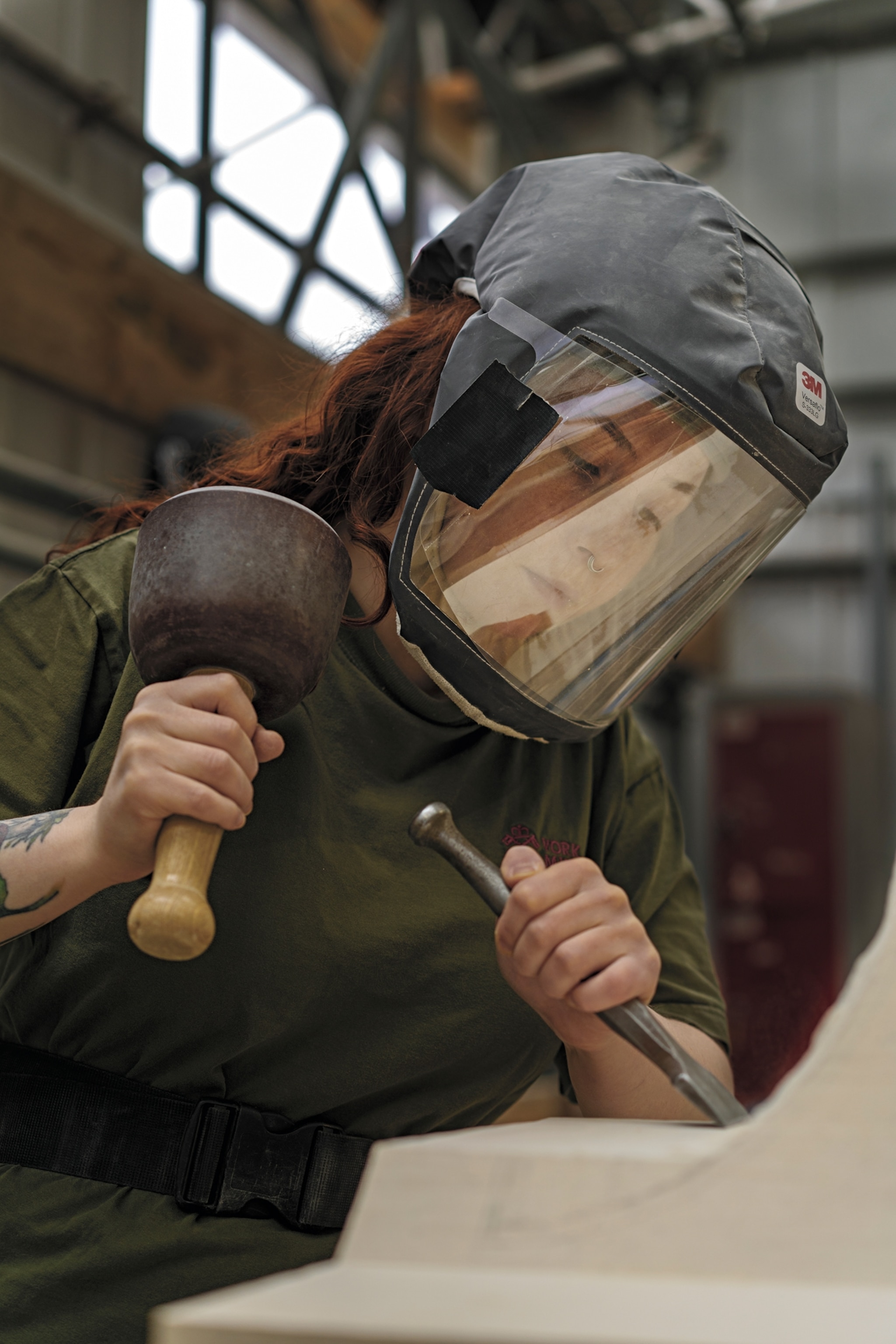 Person with face covered by protective shield working on stone with chisel and rubber mallet.