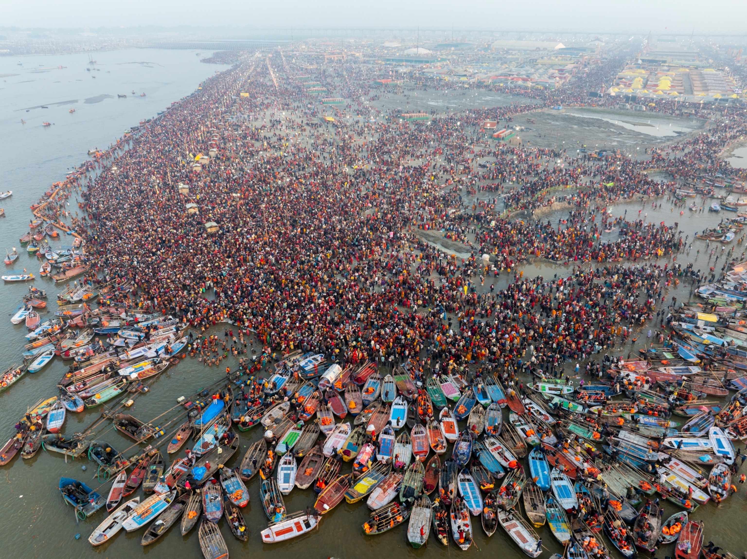 An aerial view shows a massive gathering of people by the water. Boats surround the coast.