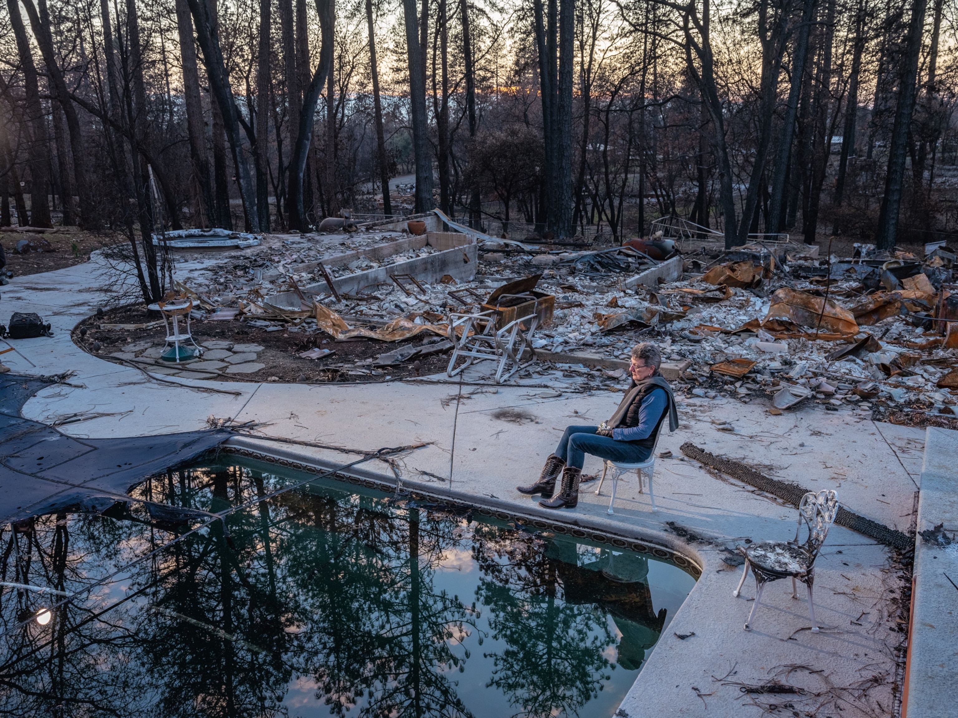 woman sitting in chair by poolside near the ruins of her home.