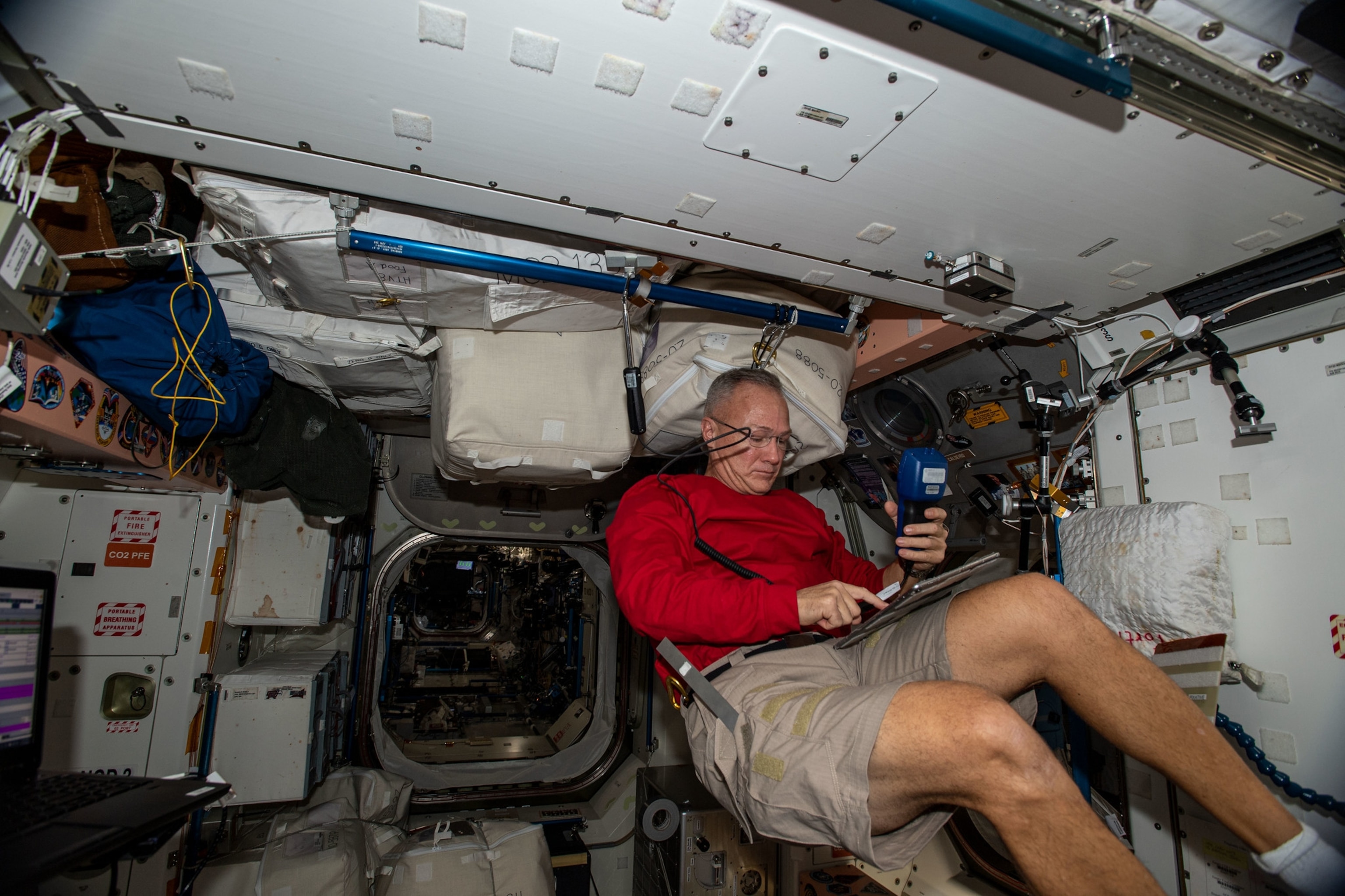 man in eye-glasses, wearing red sweater and shorts looking at equipment in his hands.