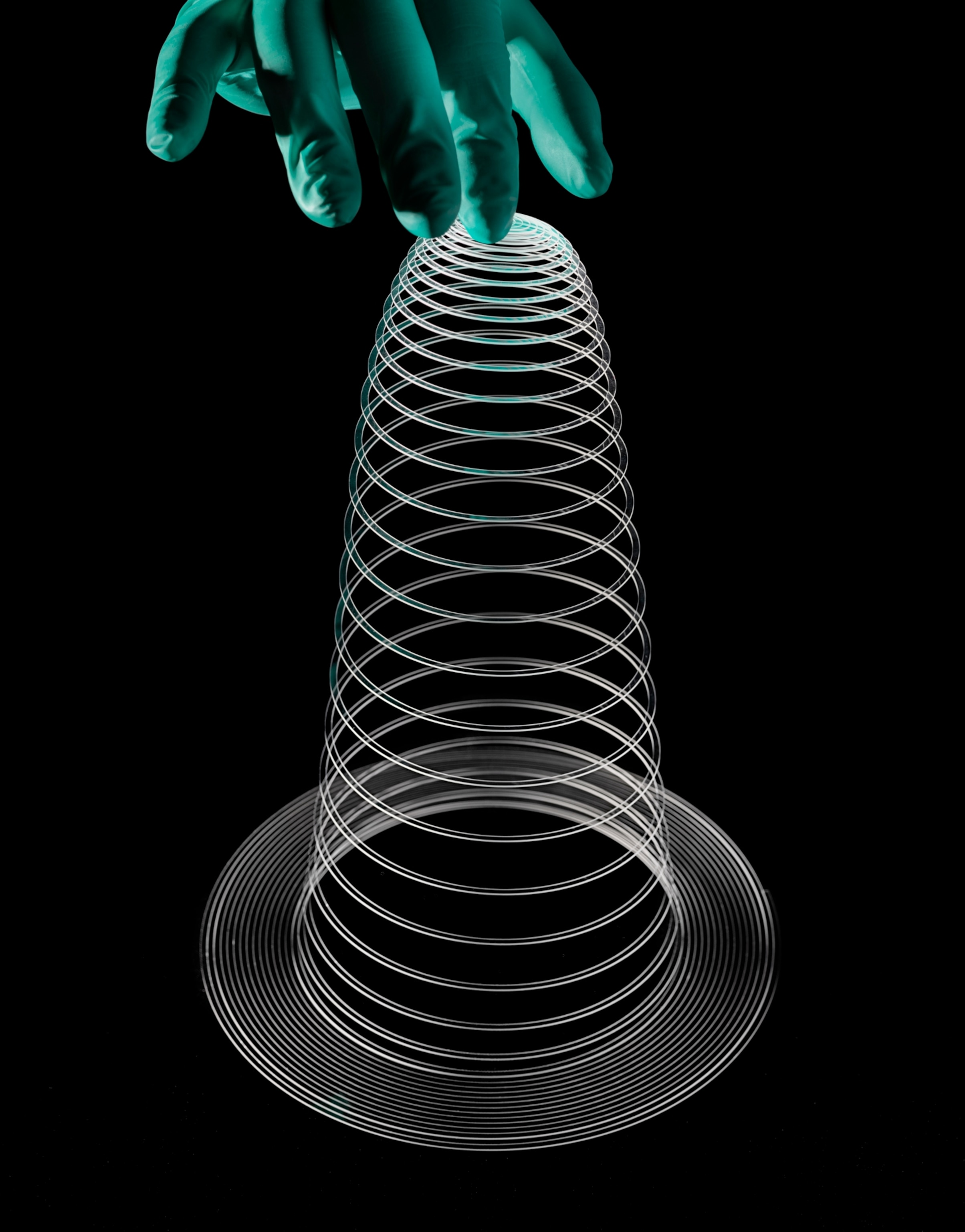 a hand in a latex glove lifts a spiral piece of glass that holds a cone and spring shape.