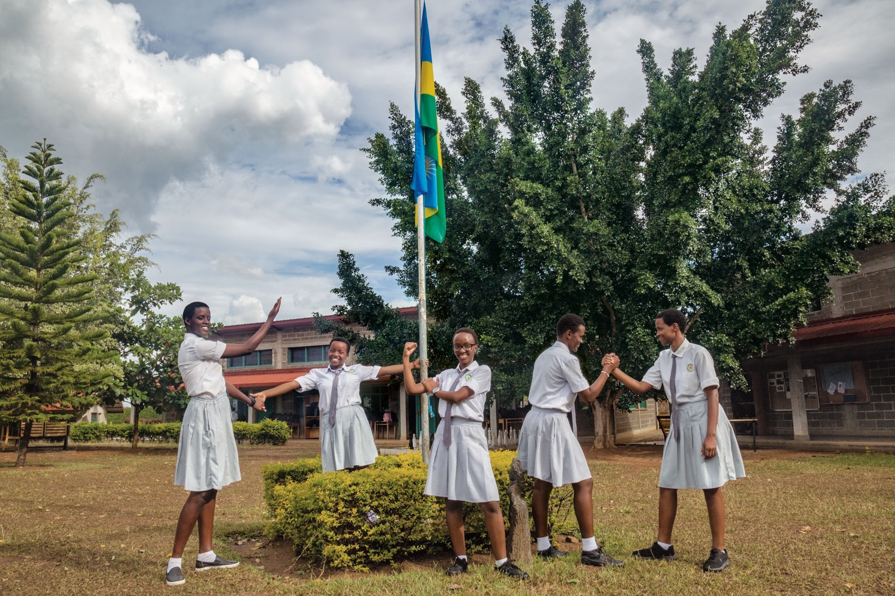 five young women posing in their school uniforms near a flag pole