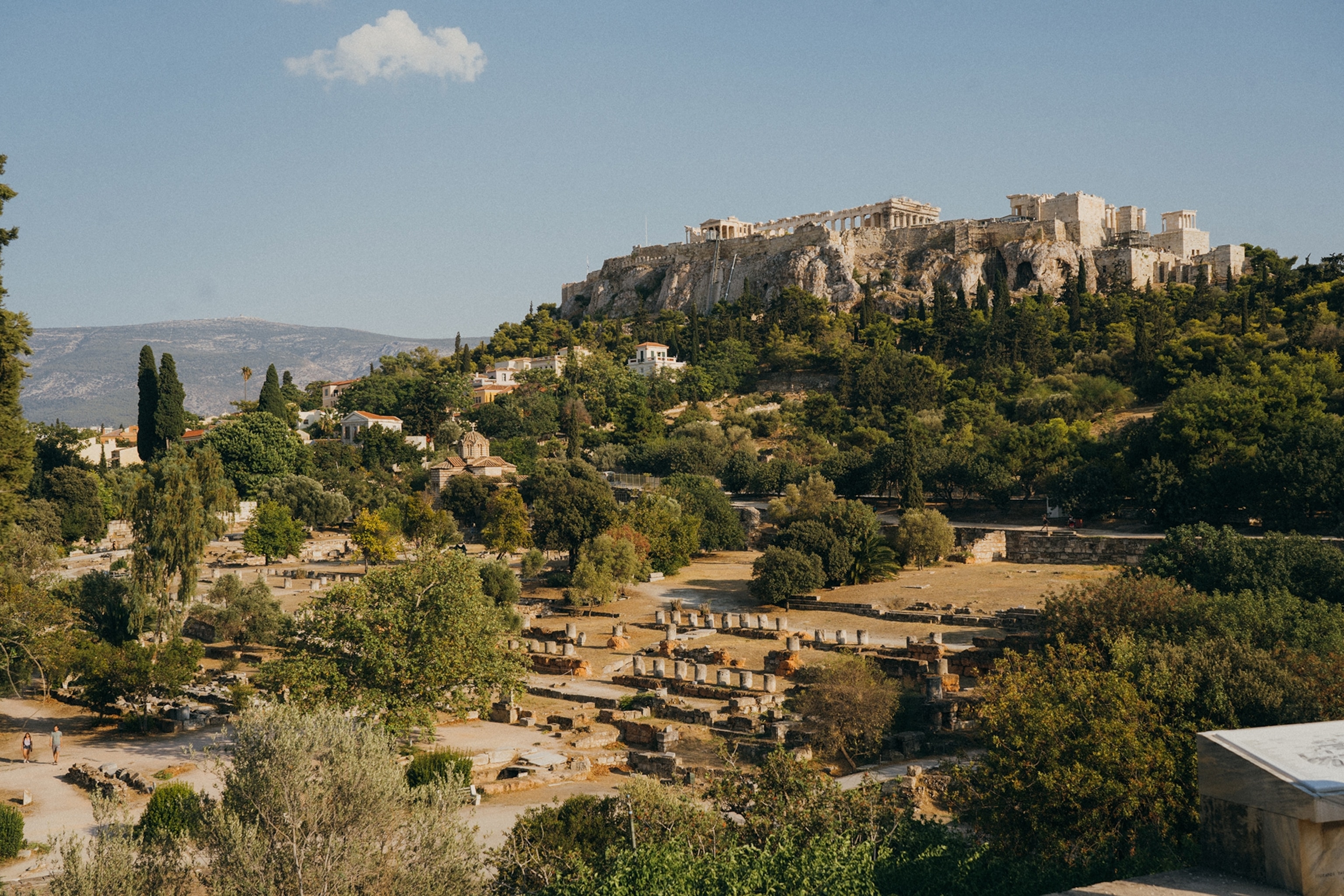 Hill adorned with trees, vegetation and historic buildings, with the acropolis perched on top