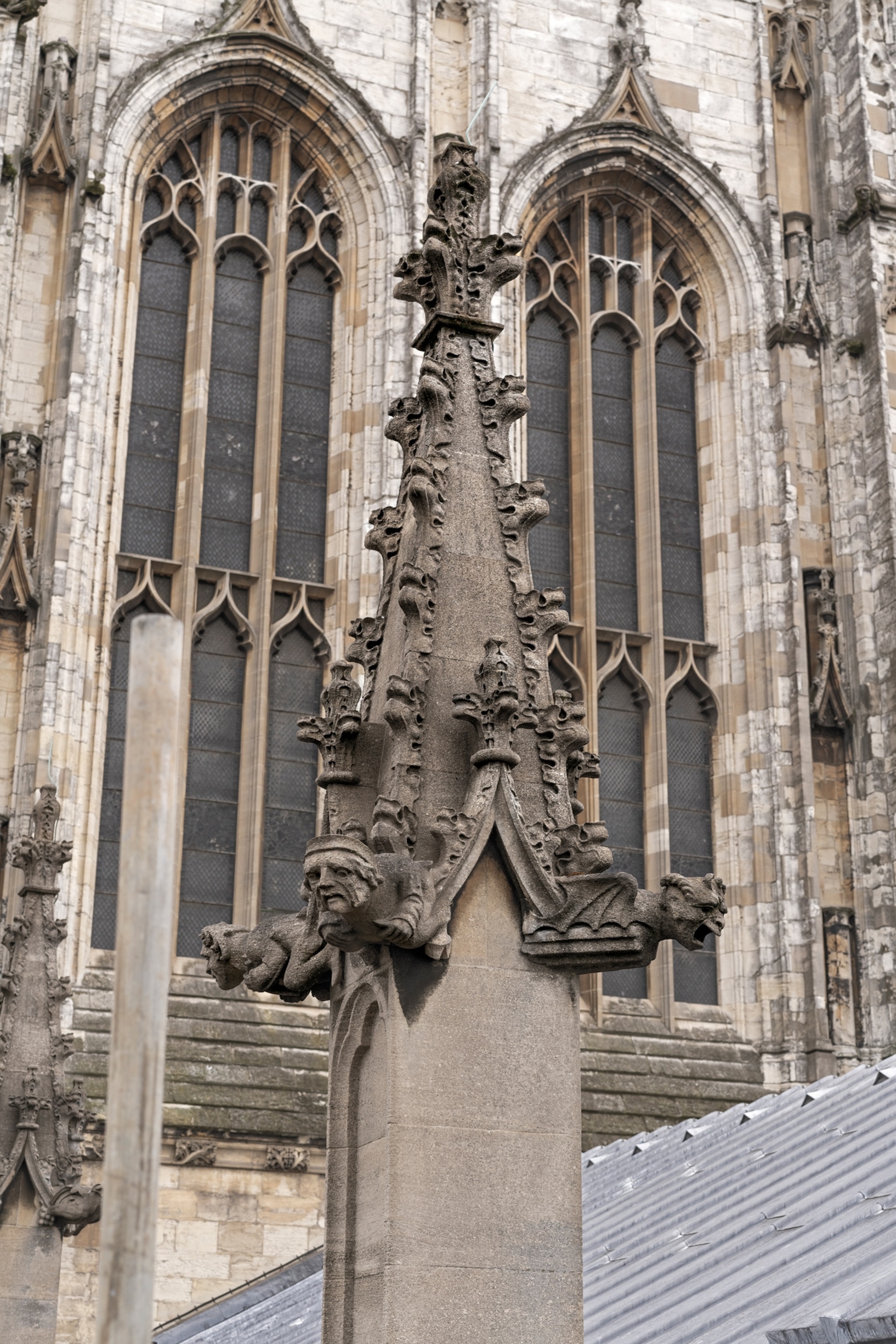 Pinnacle decorated with intricate carved gargoyles on the roof with cathedral windows on the background.