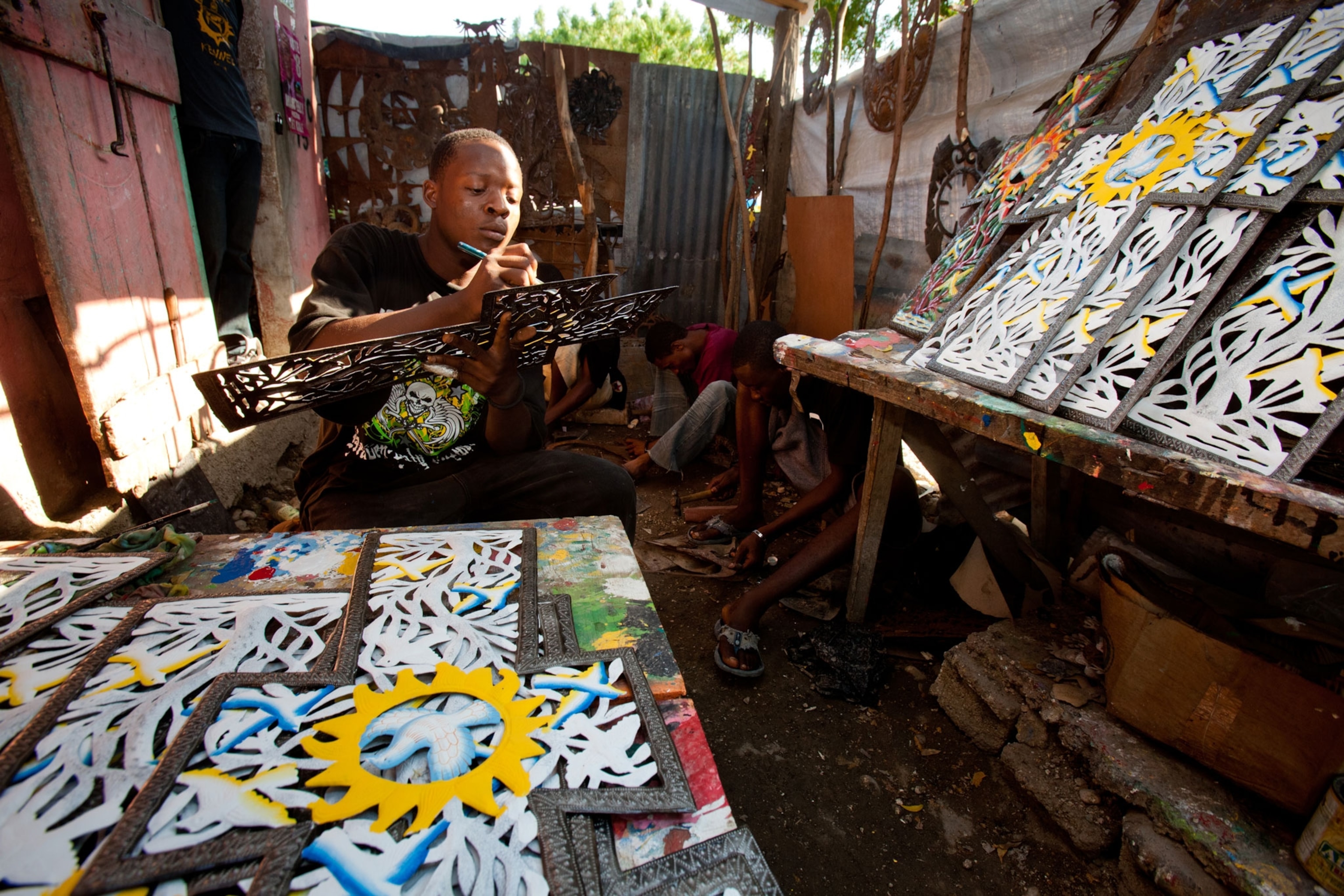 A man paints Hatian metal art to be sold to tourists.
