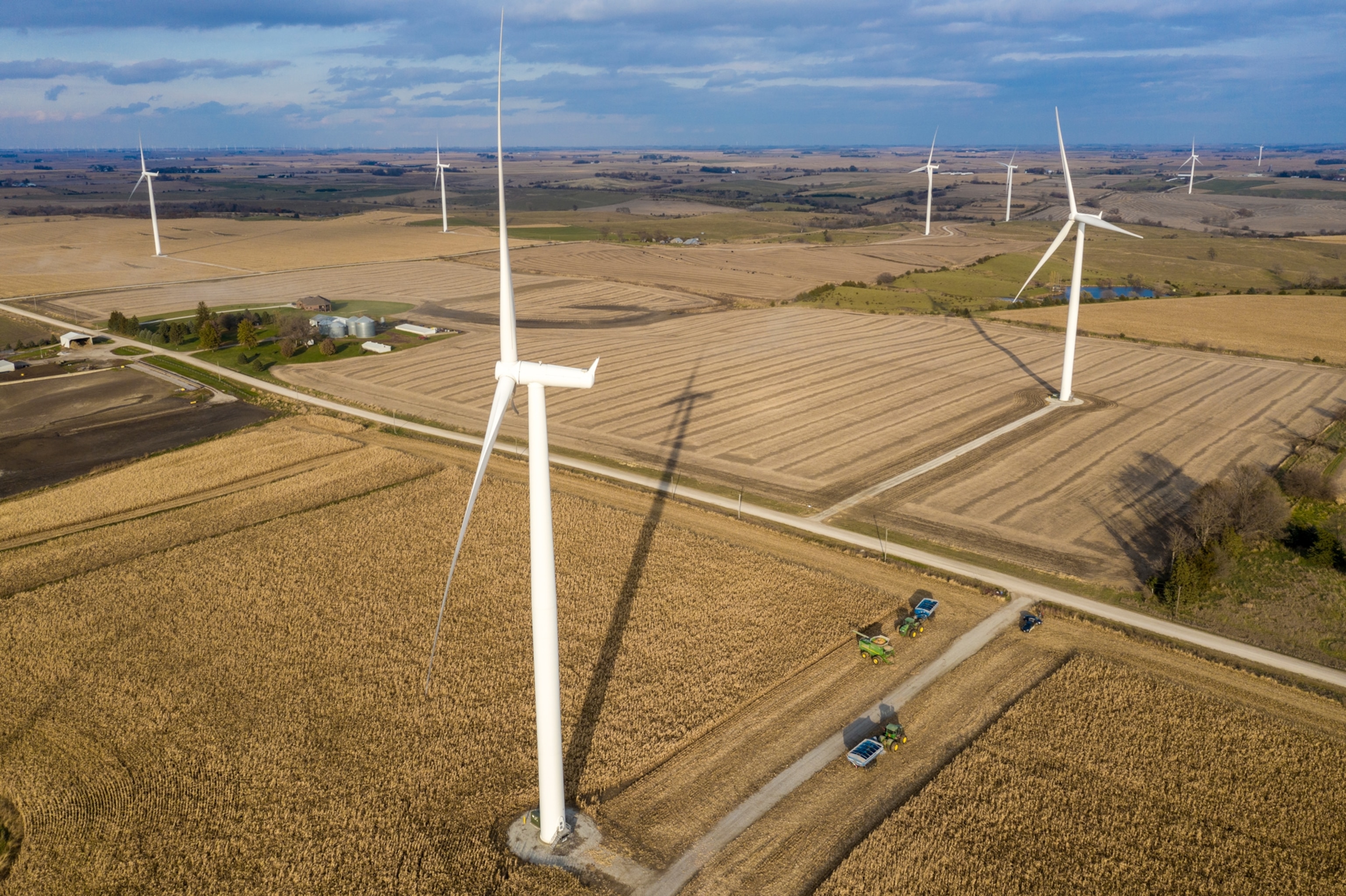 farmers harvest corn under wind turbines on their land.