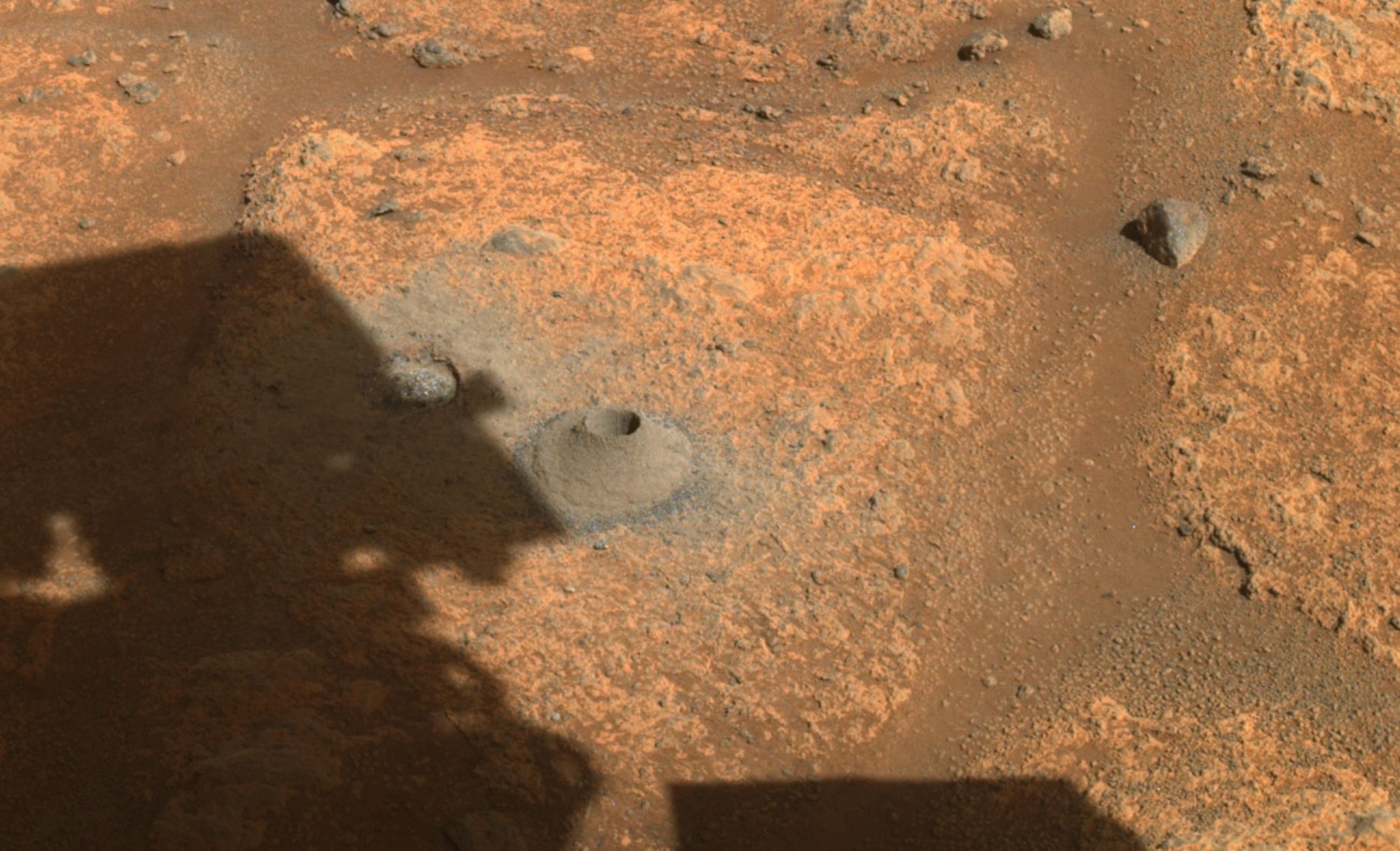 Next to NASA's Perseverance rover's shadow, there is a hole drilled in a Martian rock.