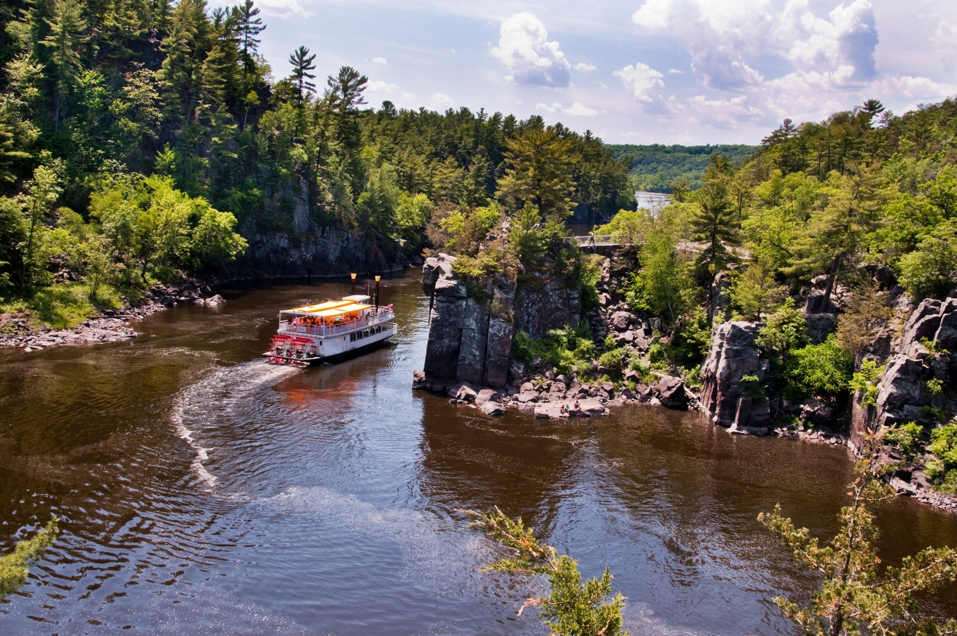 A Paddle Boat travels down the scenic St. Croix River with cliffs and trees bordering the river.