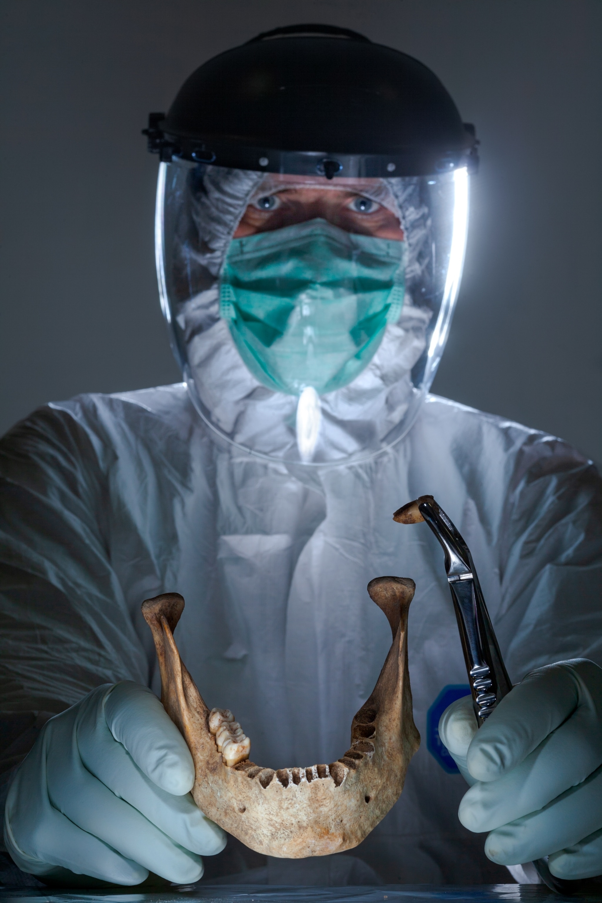 person in bio-suit and mask holding a low jaw bone.